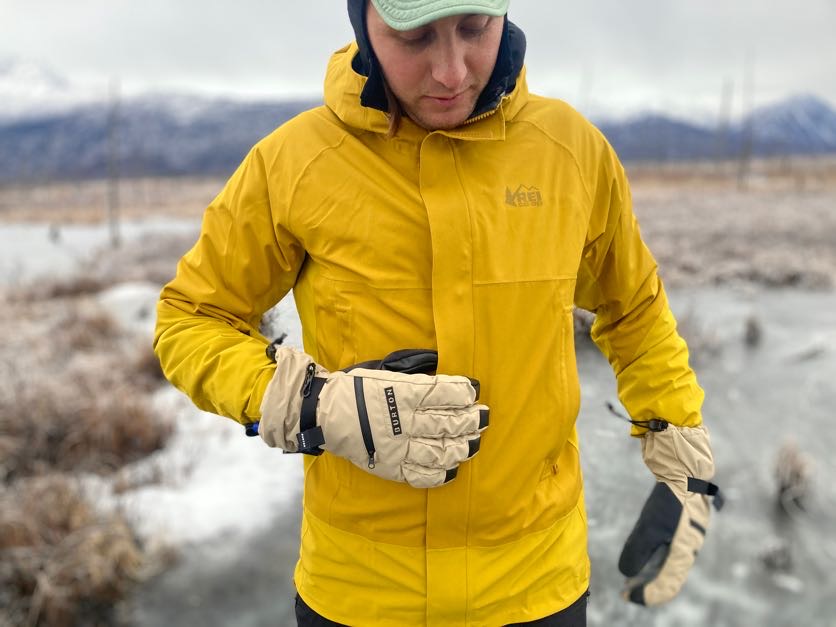 A man reaches for the zipper of his jacket while wearing winter gloves.