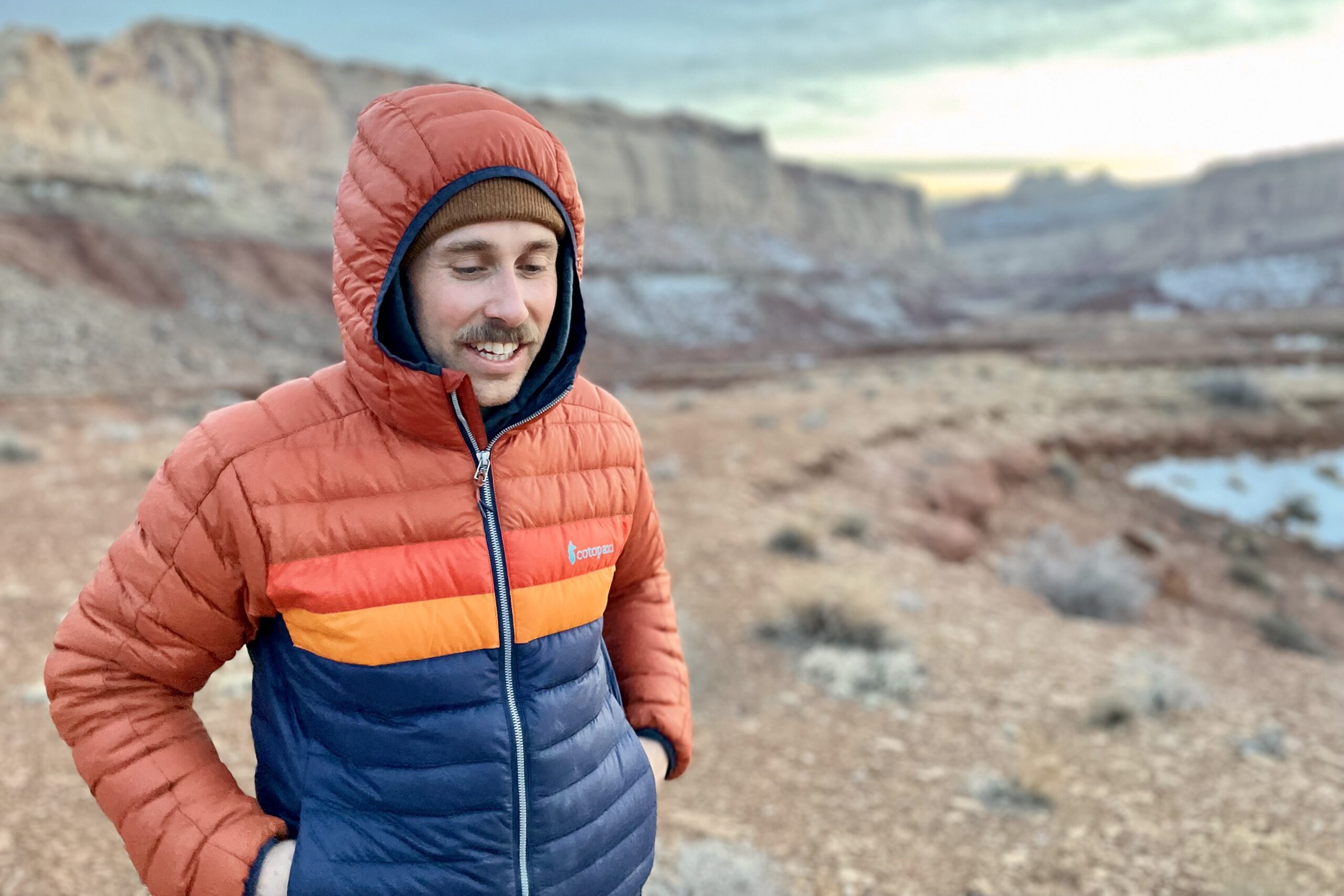 A man in a puffy jacket smiles in the desert.