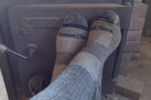 Closeup looking forward at feet wearing the Wrightsock Silver Escape socks resting near a wood stove.