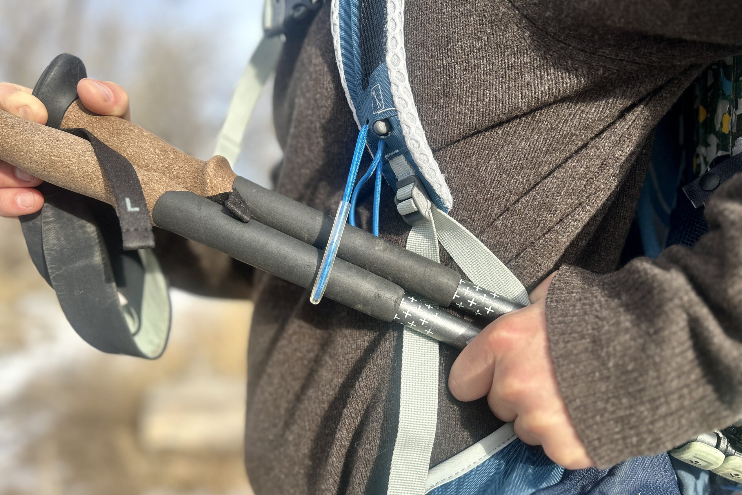 Close up of a person attaching their trekking poles to their daypack.