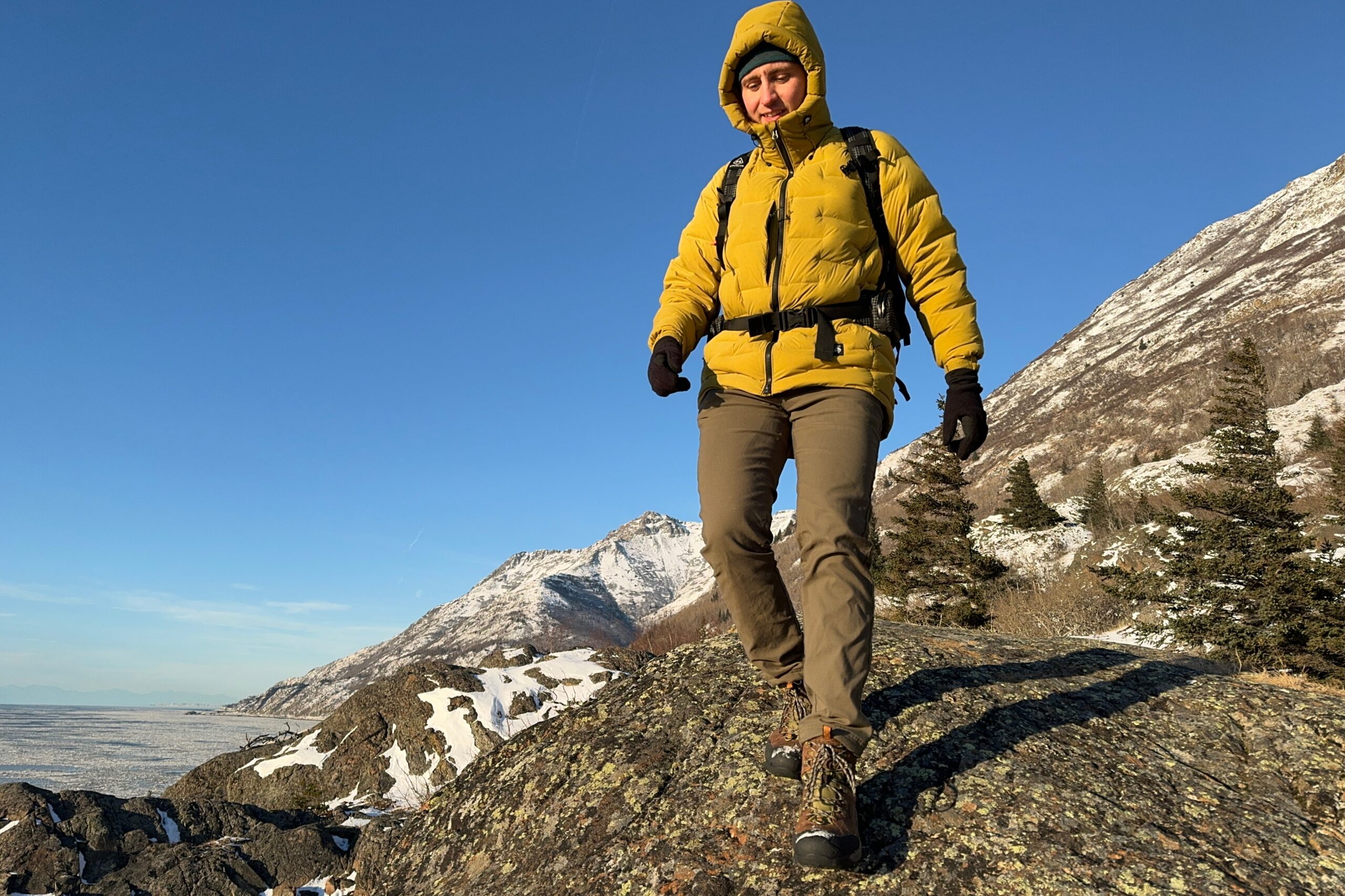 A man walks down a rocky ridge over an ocean view in the winter.