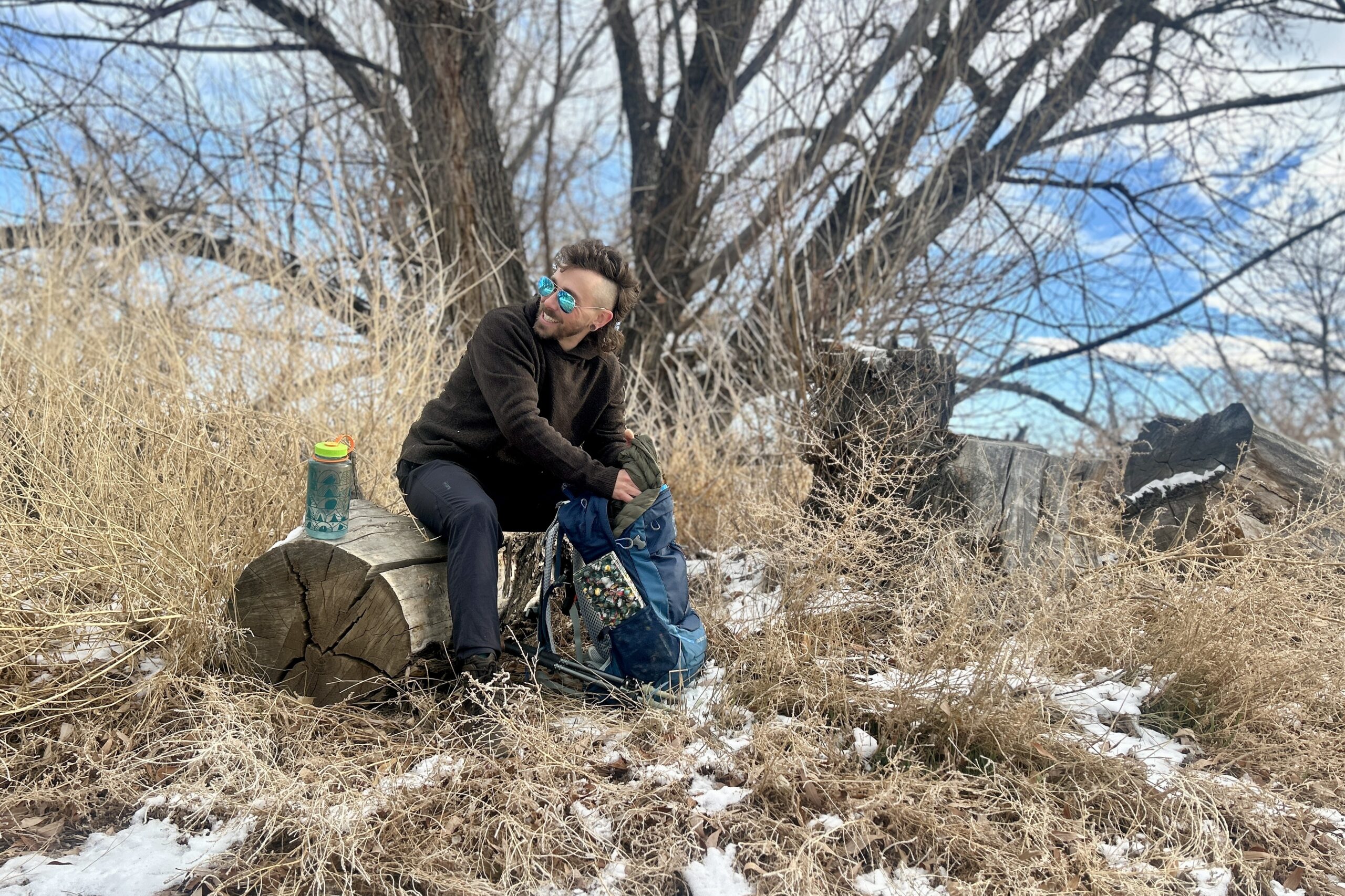 A man goes through the contents of his daypack while sitting on a log and smiling.