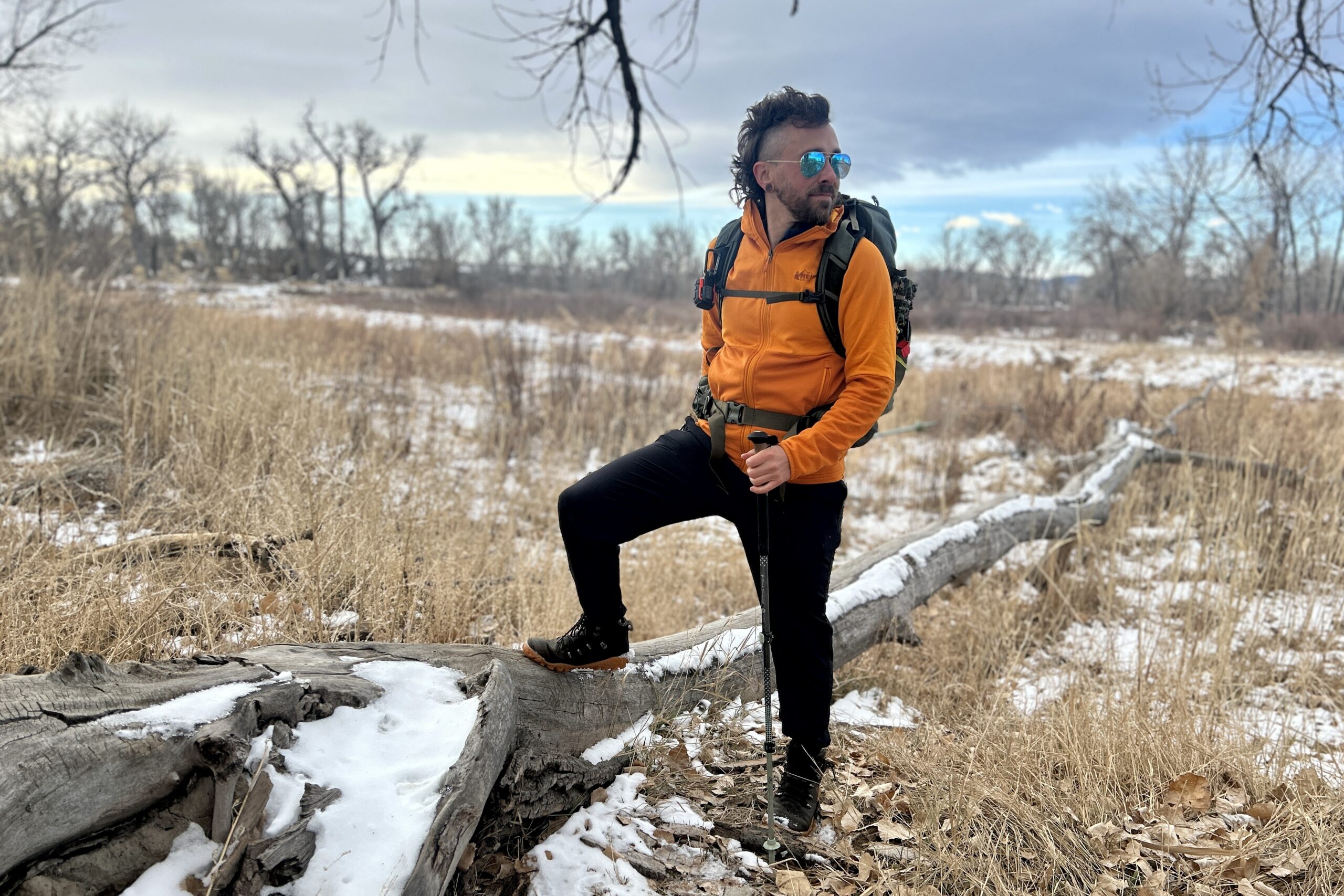 A man poses with a big backpack on and looks in the distance in a snowy wilderness area.