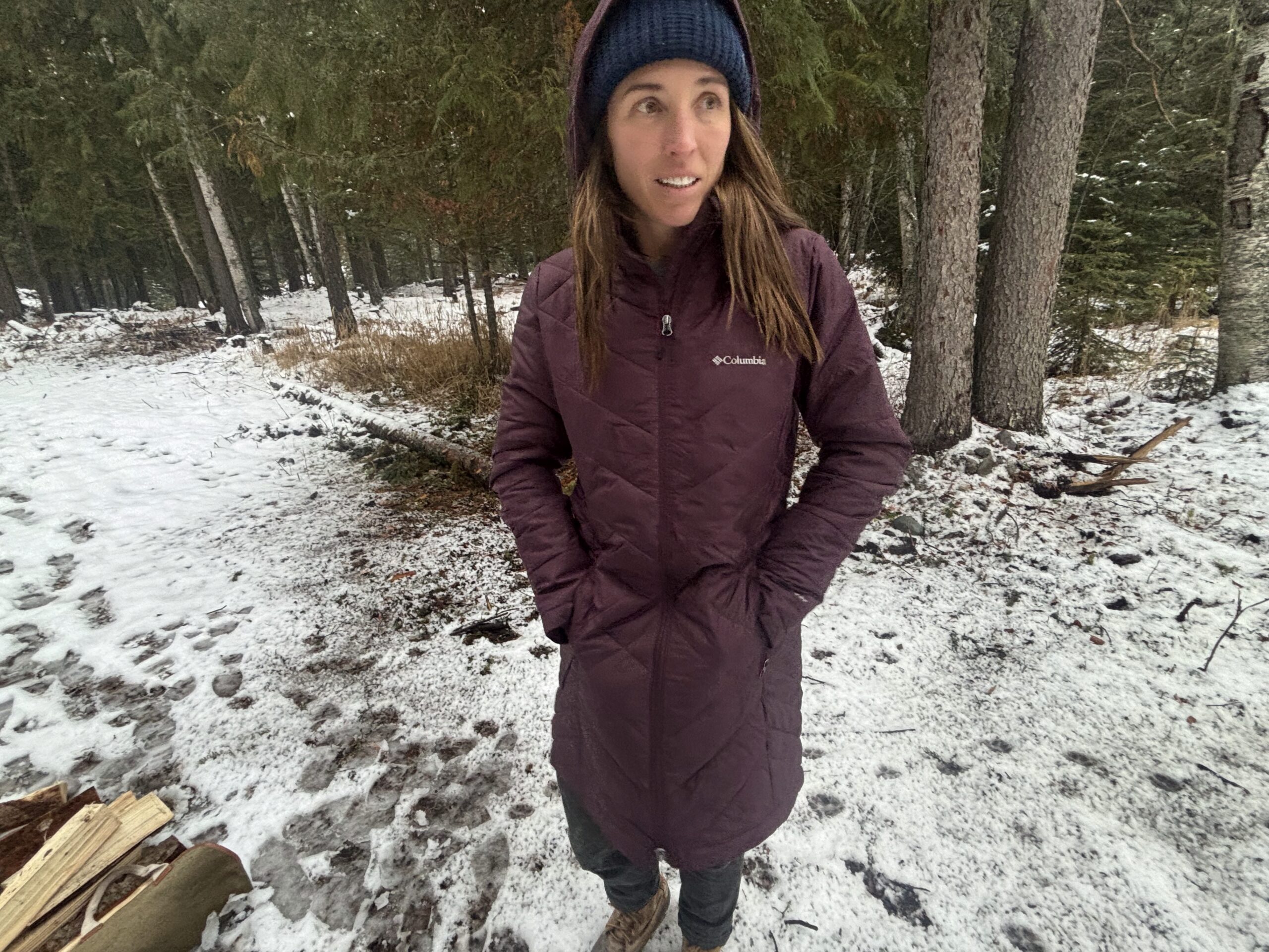 a women standing in a wooded area with her hands in the pockets of the columbia heavenly long jacket with the hood up