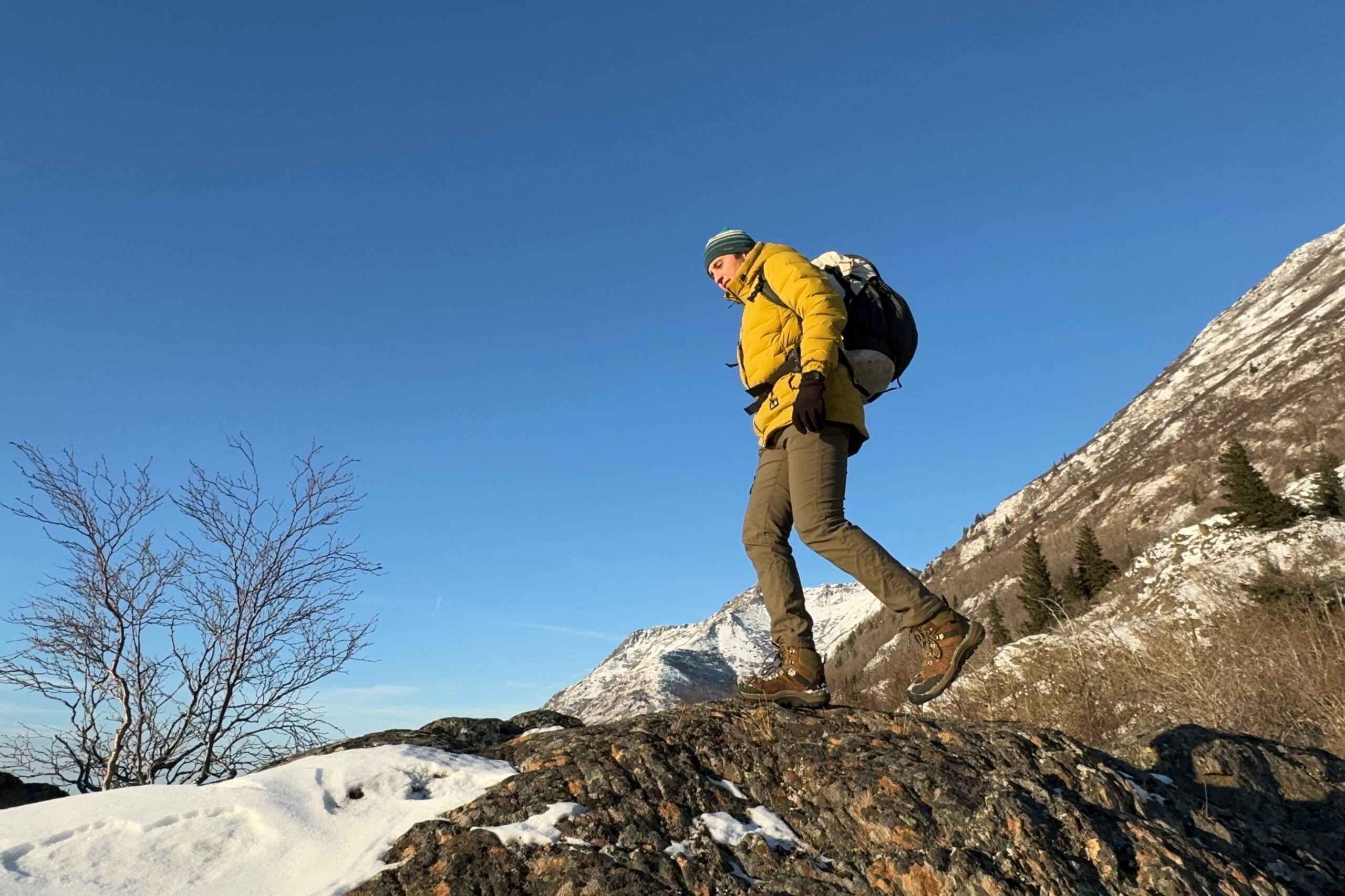 A man walks down a rocky outcrop with mountains in the background.