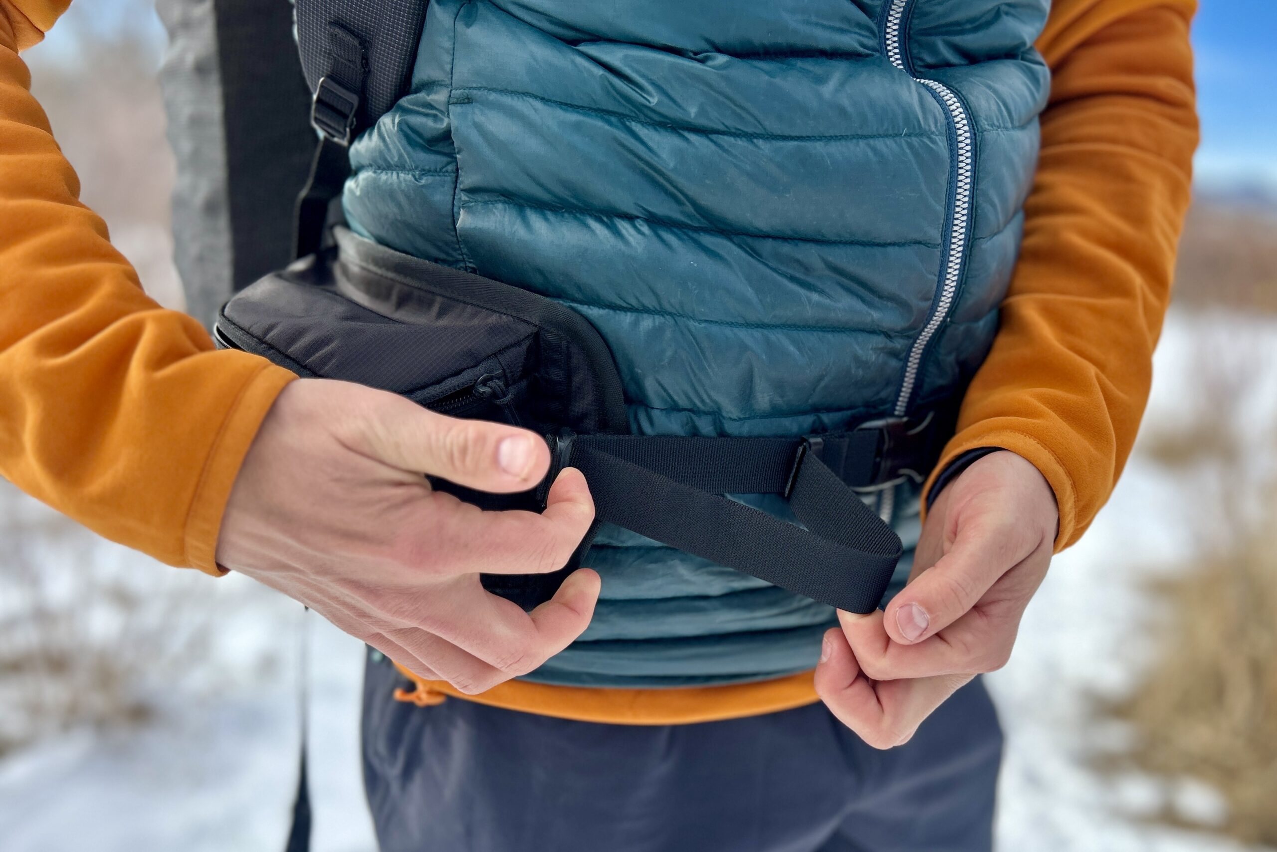 Close up image of a person tightening a backpacks' waist strap.