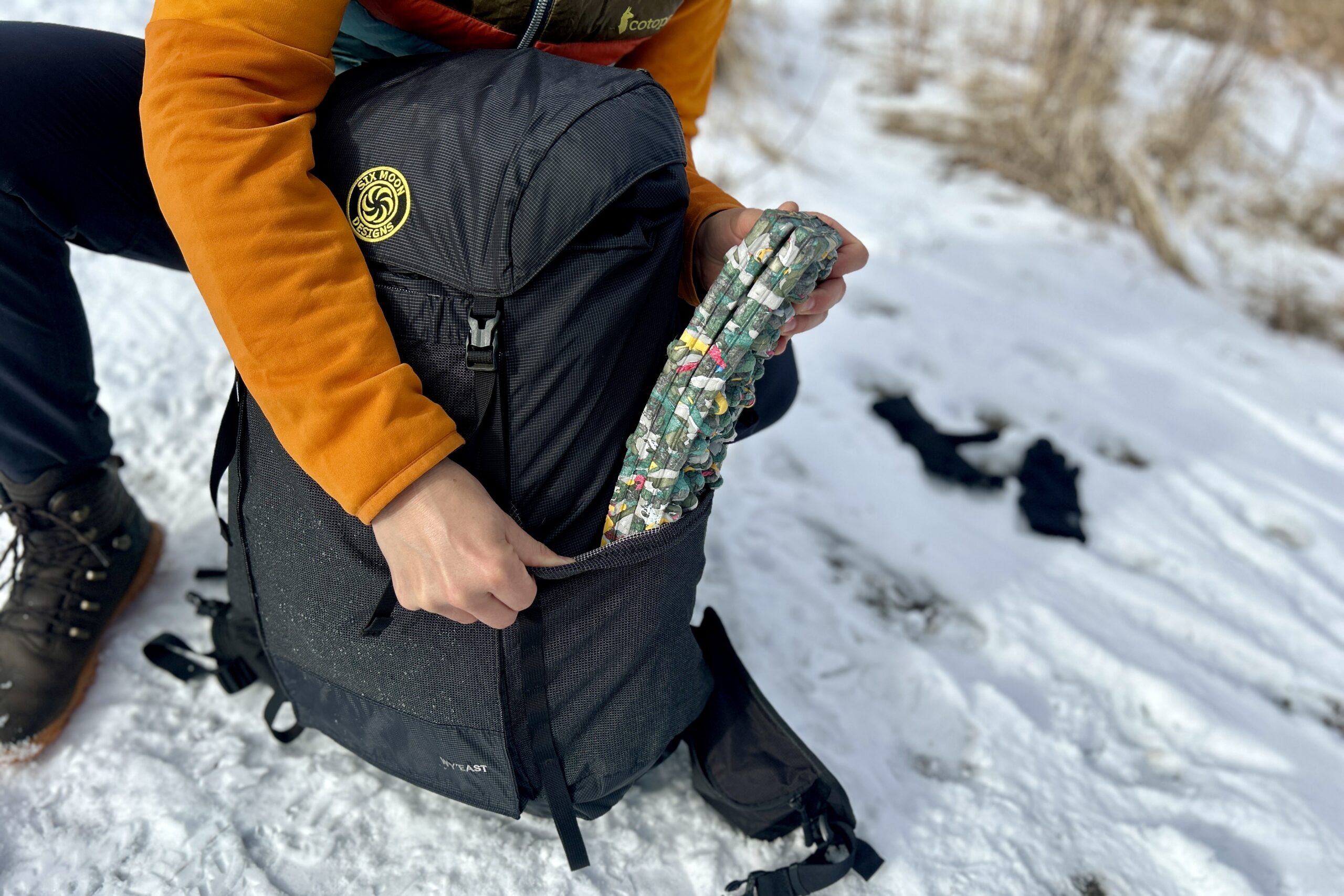 Close up image of a person removing a sit pad from the side pocket of a backpack.