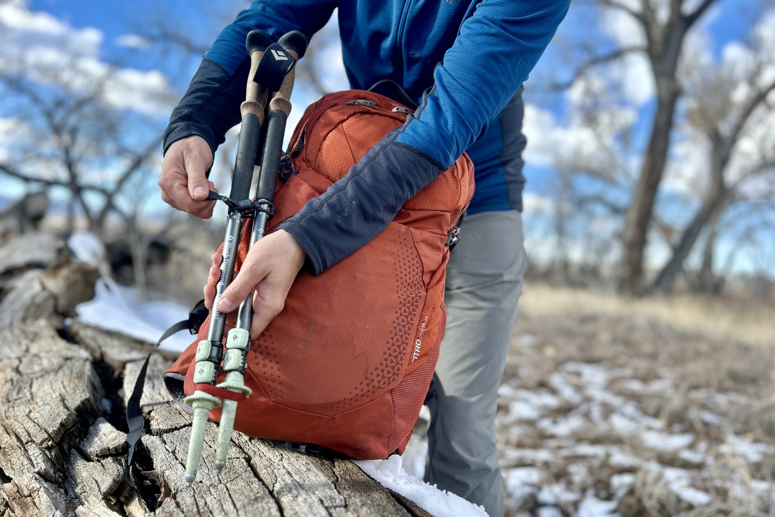 A person attaches hiking poles to a daypack.