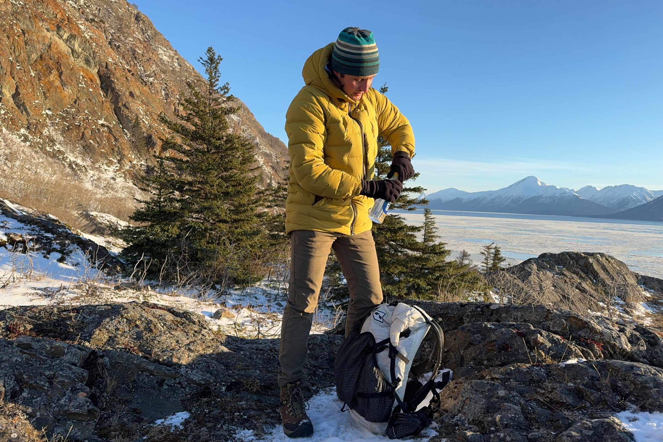 A man puts a water bottle in his backpack on a rocky ridge.