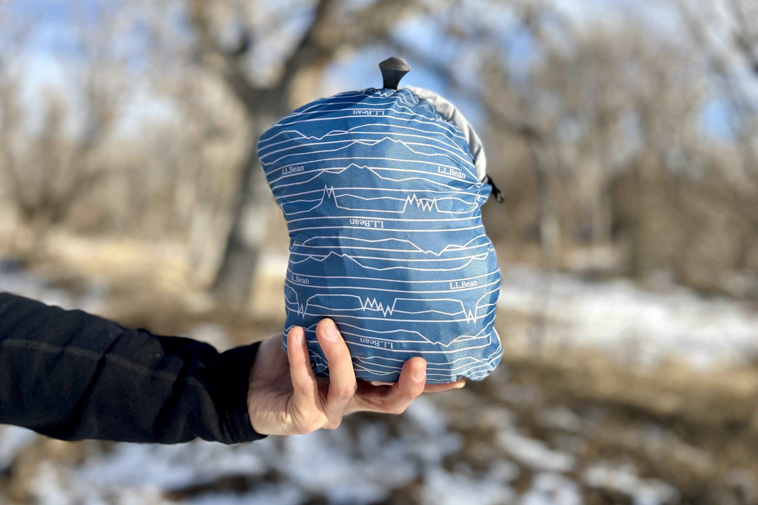 Close up of a person holding a collapsed backpack in a small zippered bag.