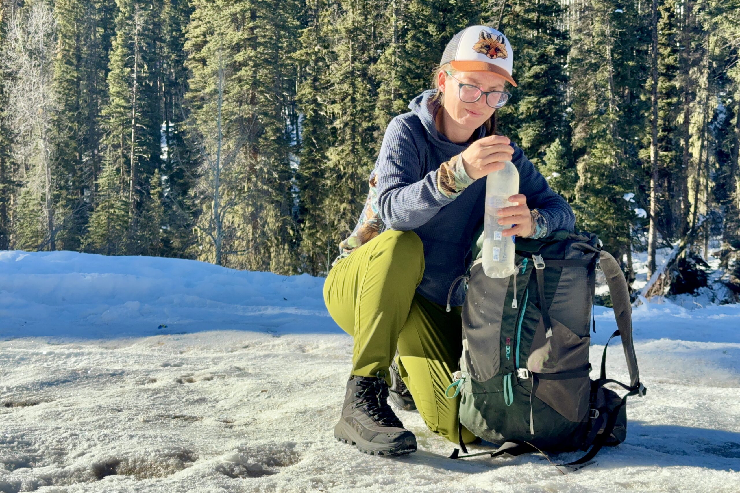 A person wearing the Thermo Chill Mids is taking a water bottle out of a backpack in the woods.