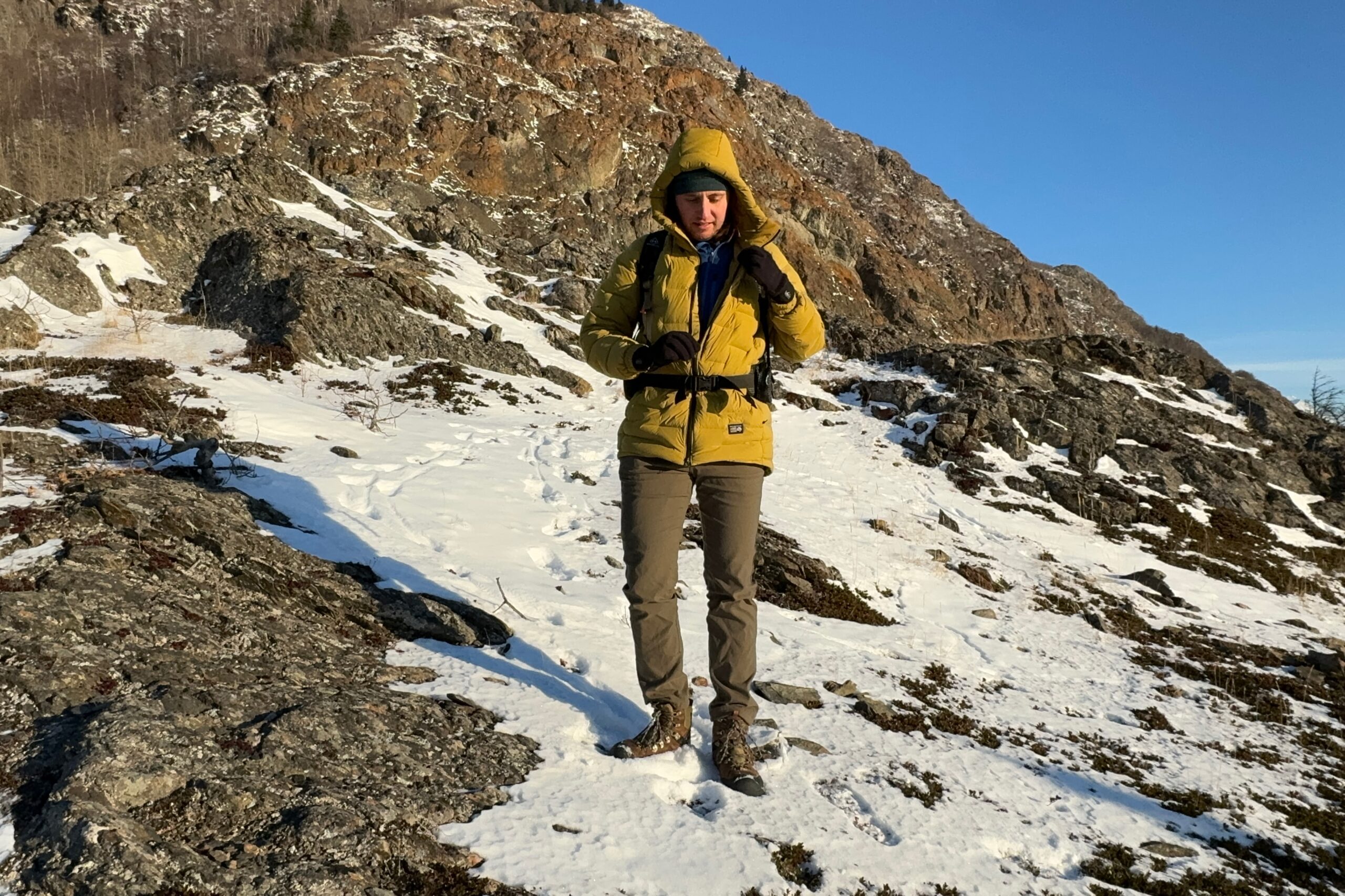 A man unzips a yellow jacket on a rocky hillside.