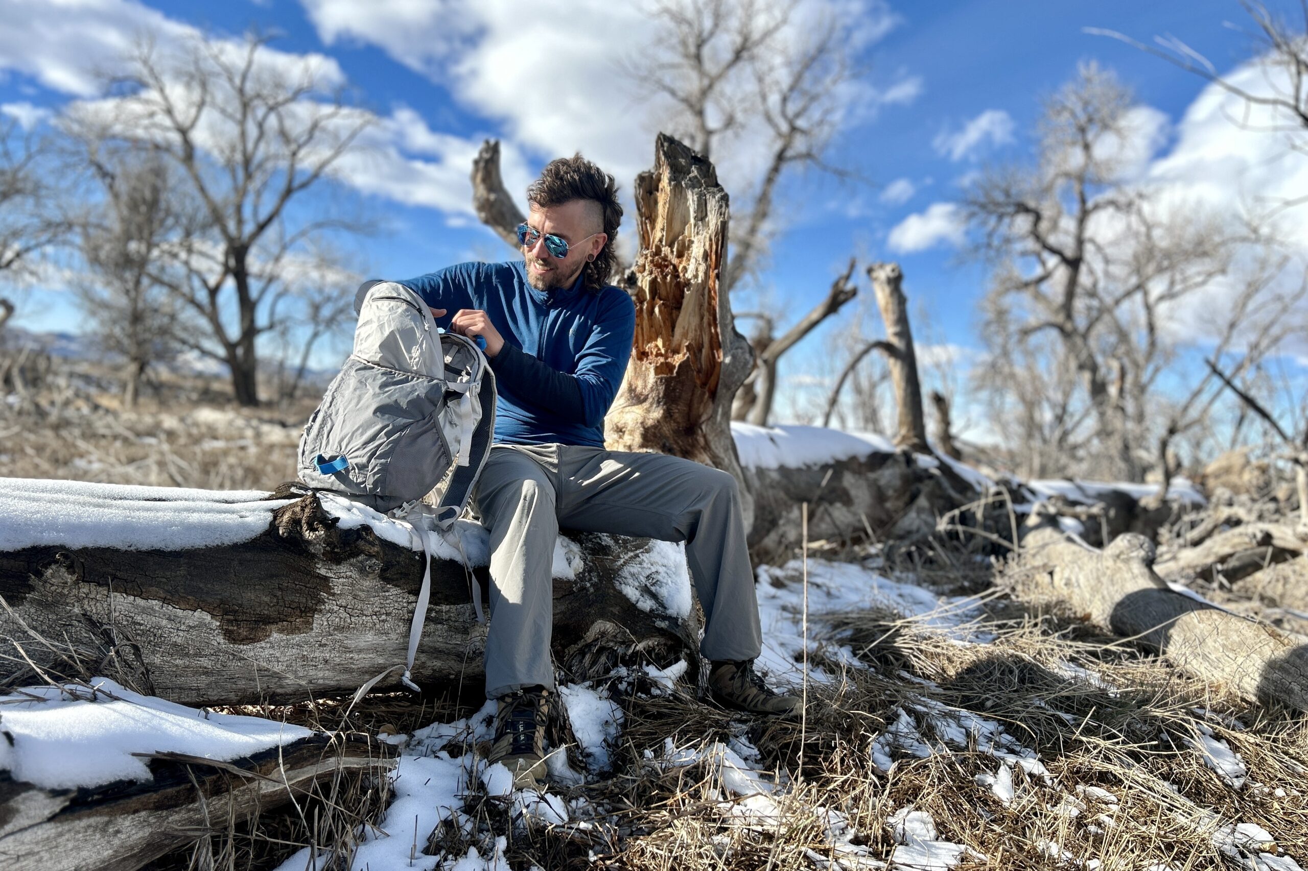 A man sits on a log in a wilderness area and digs through the contents of his daypack.