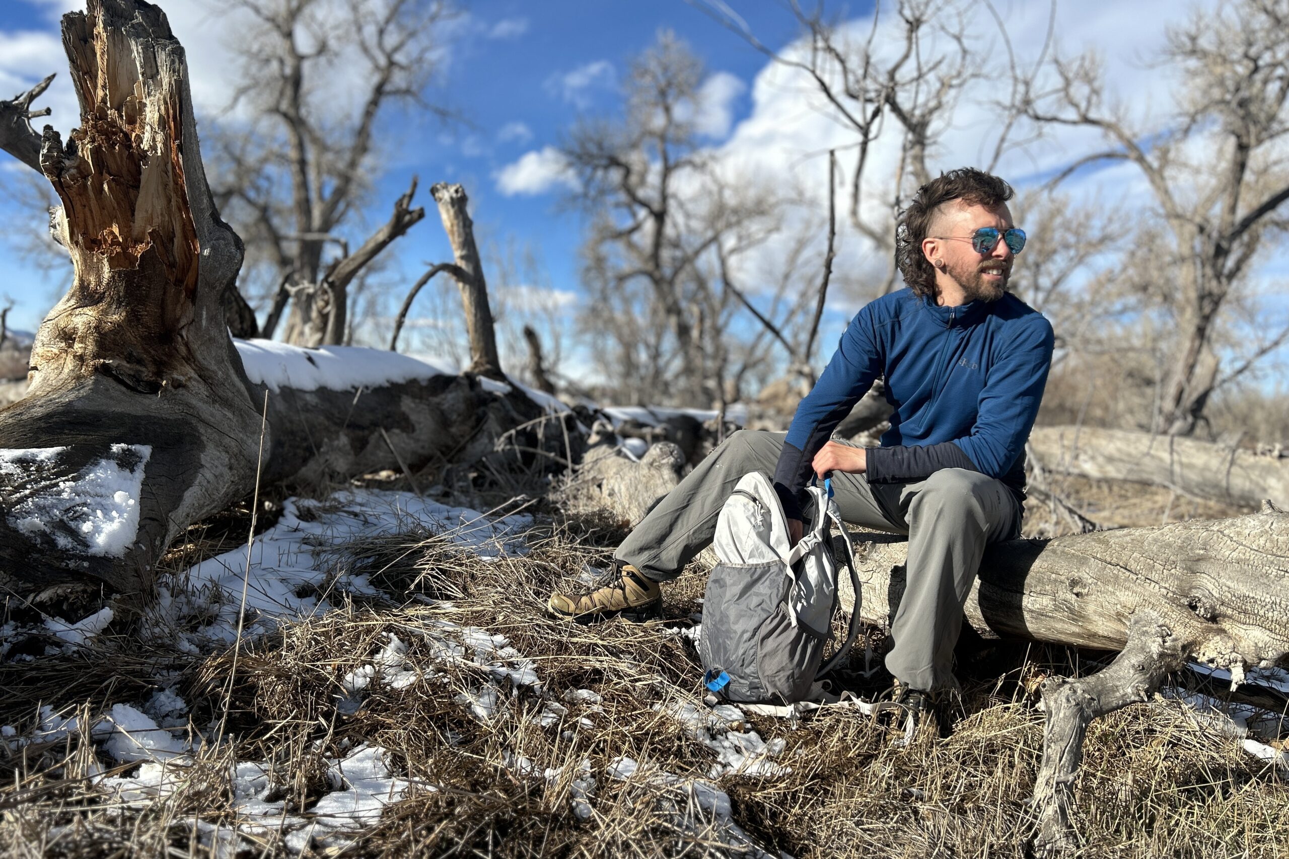 A man sits on a log in a wilderness area and digs through the contents of his daypack.