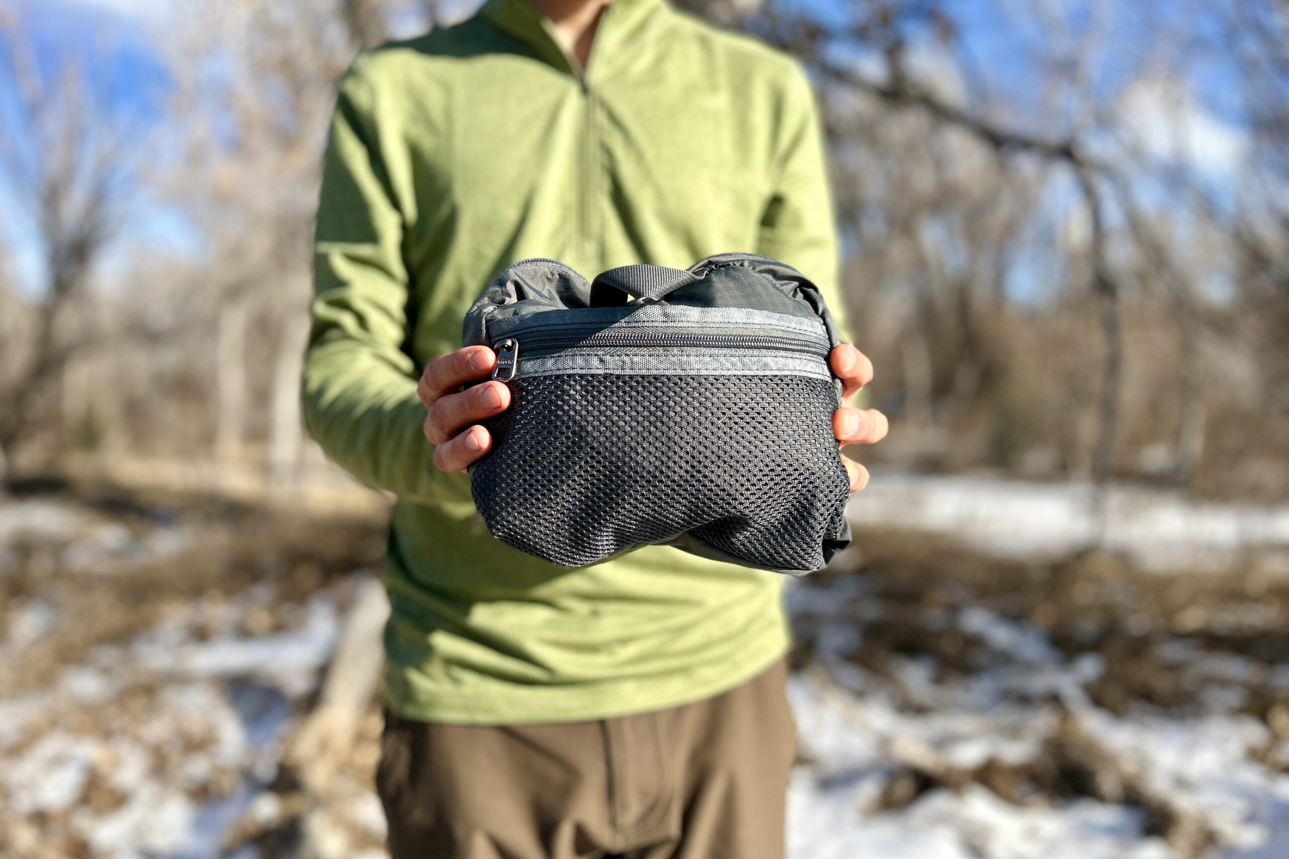 Close up of a person holding a collapsed backpack in a small zippered bag.