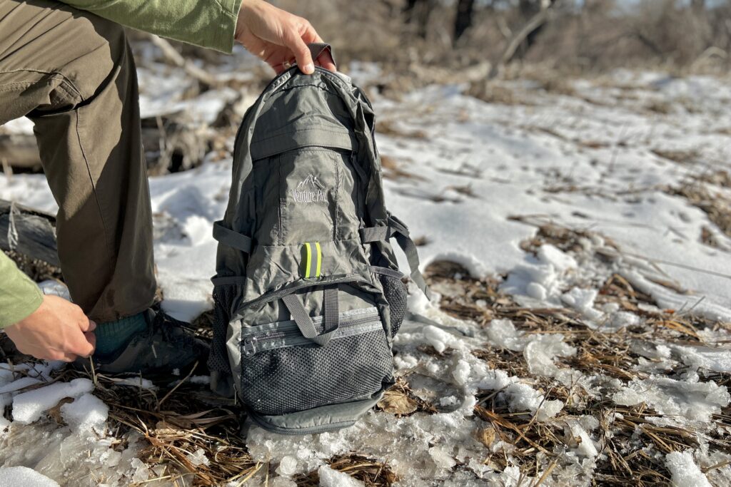 Closeup of a person holding up a daypack in a wintry forest landscape.