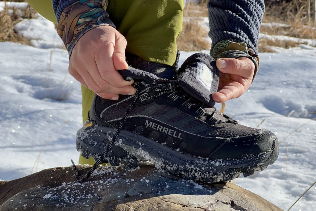 A close up of a person showing the inside of the Thermo Chill Mid boots on a rock in the snow.