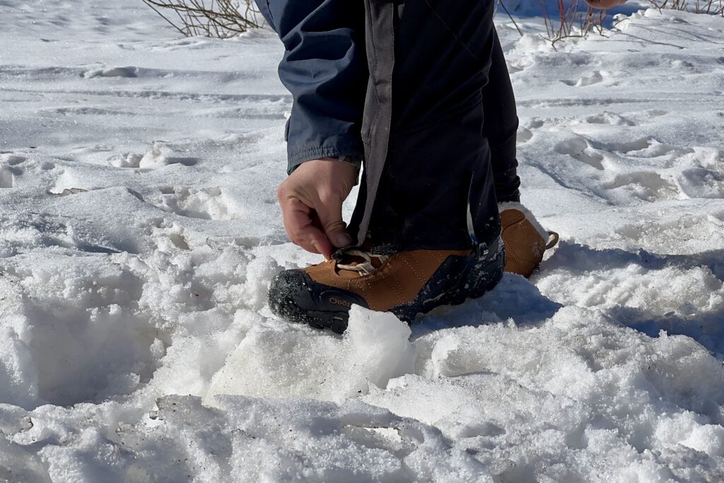 A close up of a person attaching some gaiters to the Bridger boots in the snow.