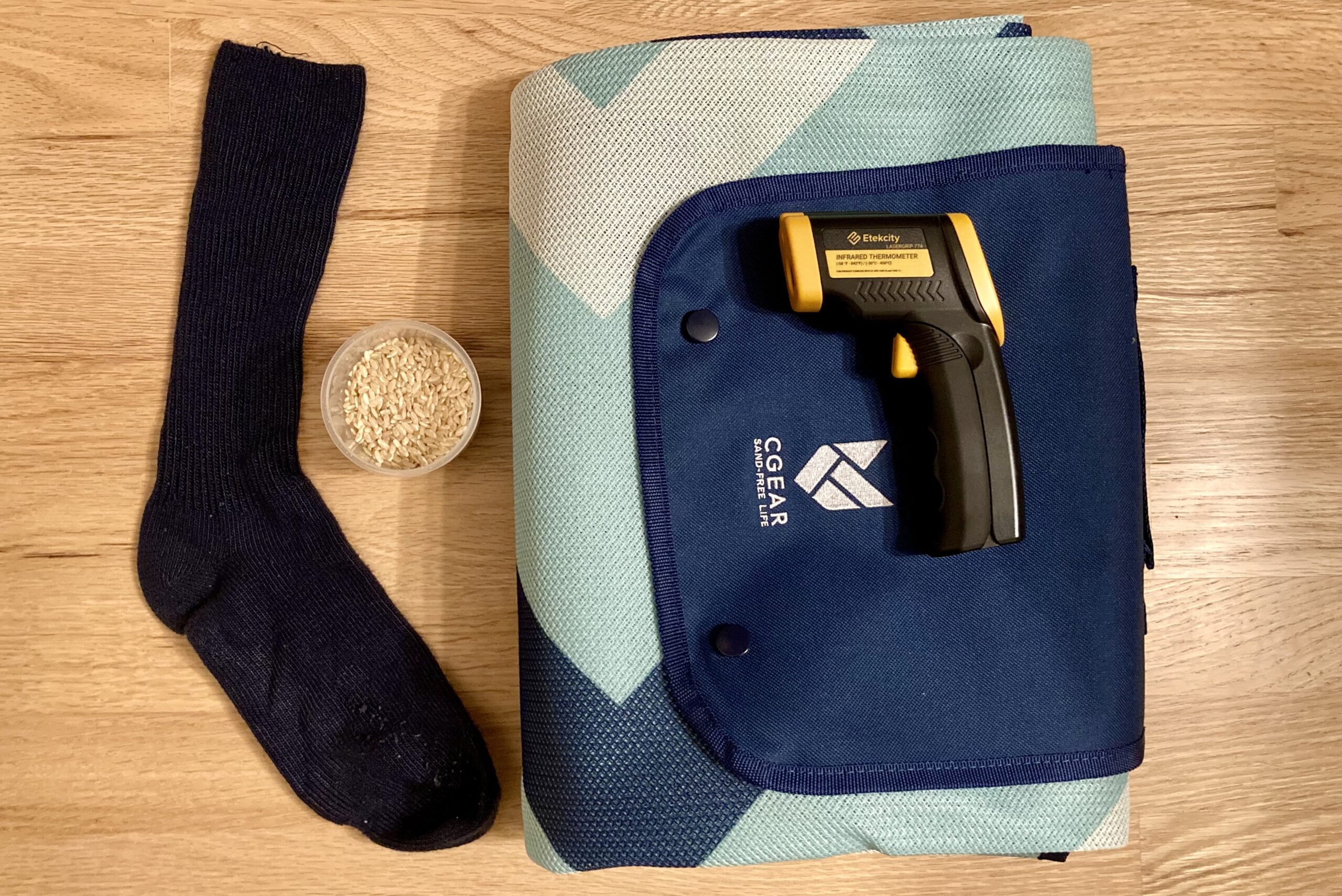 Close-up displaying the tools used in our warmth test for the CGear Multimats Sandlite Sand-free Mat: rice to put inside of a sock (for a hot sock) and the infrared thermometer.