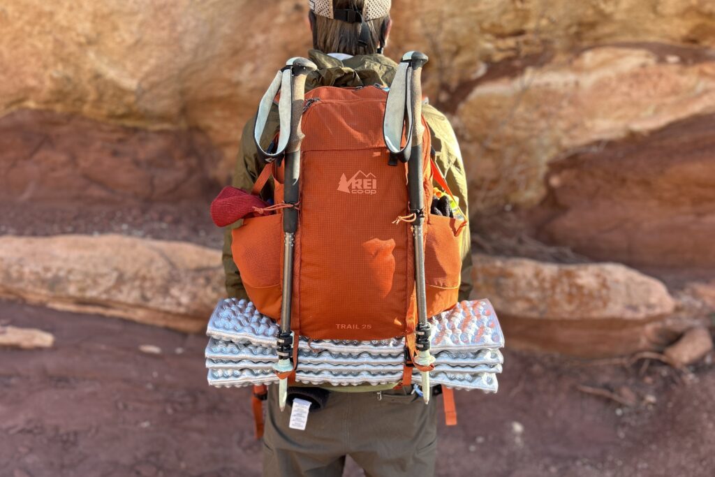 Closeup image of a man wearing a backpack with a foam sleeping pad on the bottom and two hiking poles attached.