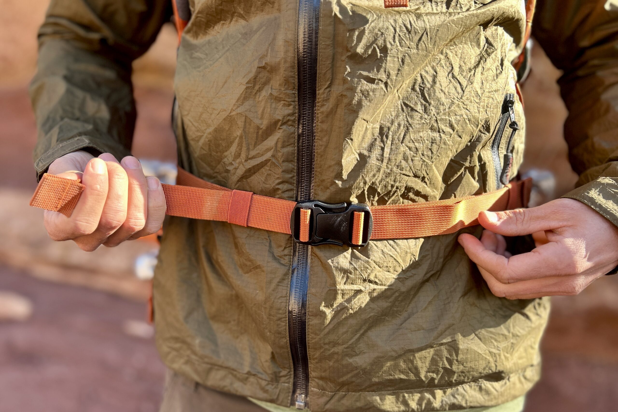 Closeup image of a man adjusting the waist strap of a backpack.