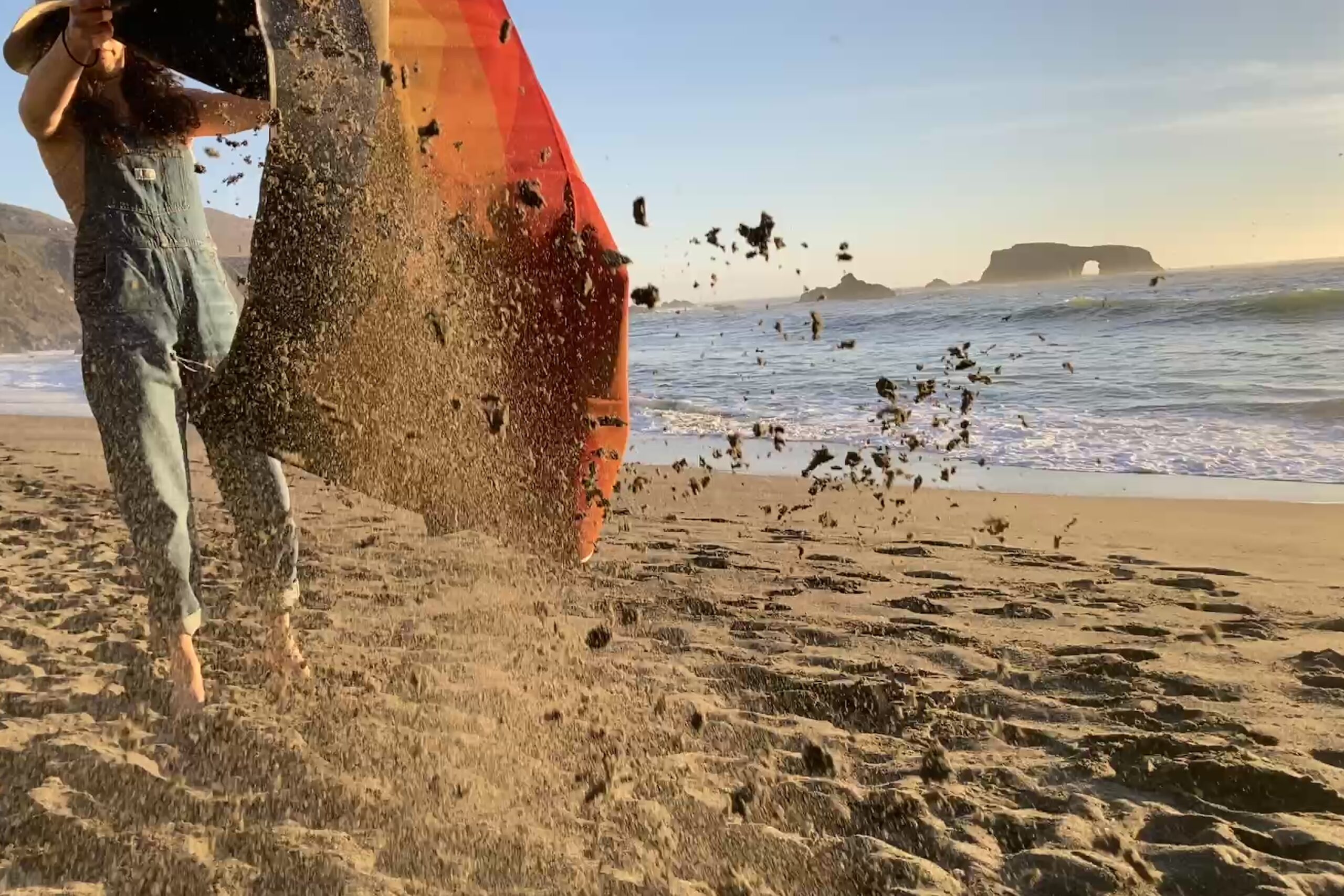 Person shaking sand off of the Nemo Victory Patio Blanket at the beach.