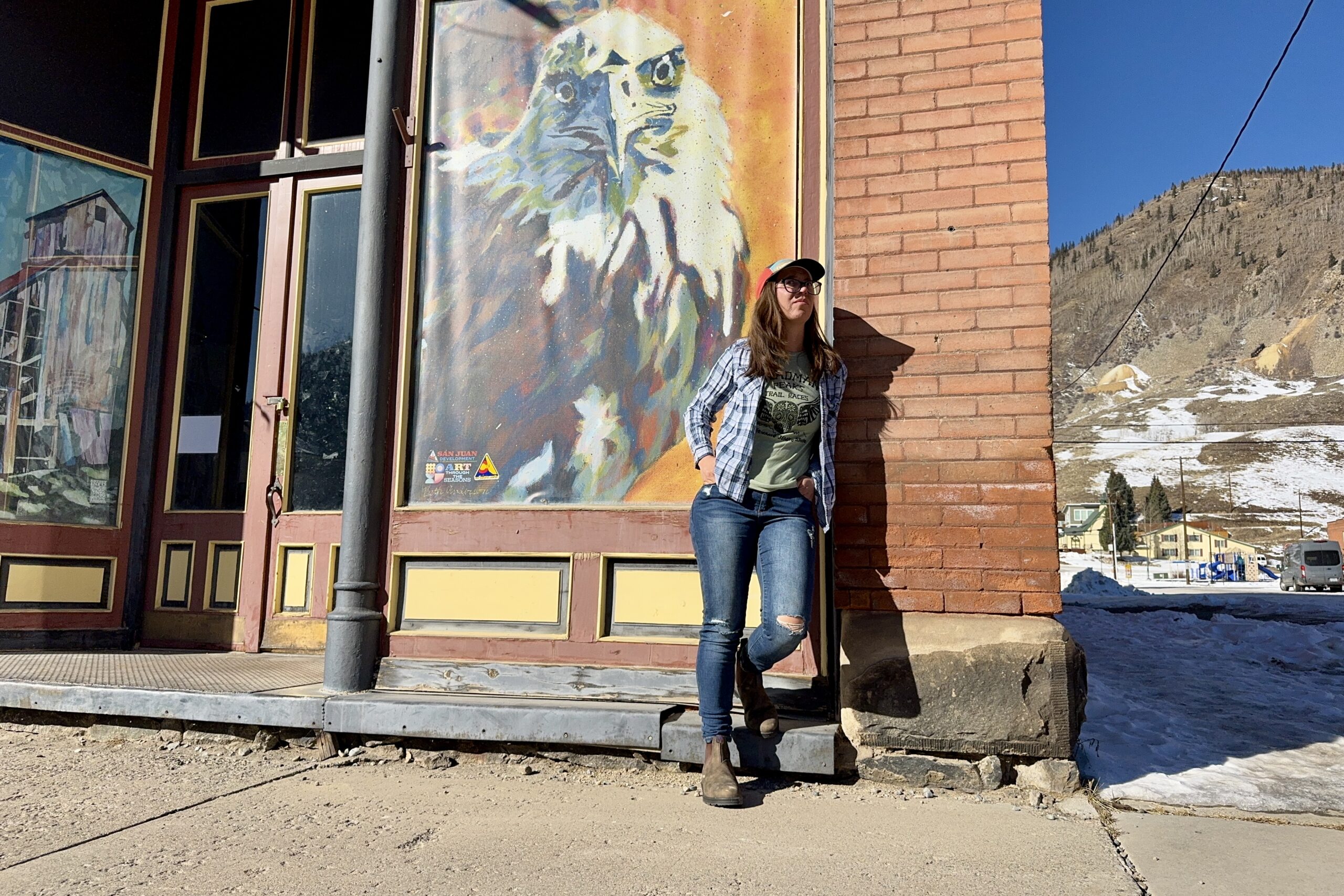 A person wearing the Blundstone Thermal Chelsea boots leans against a wall with a painting of an Eagle in a mountain town.