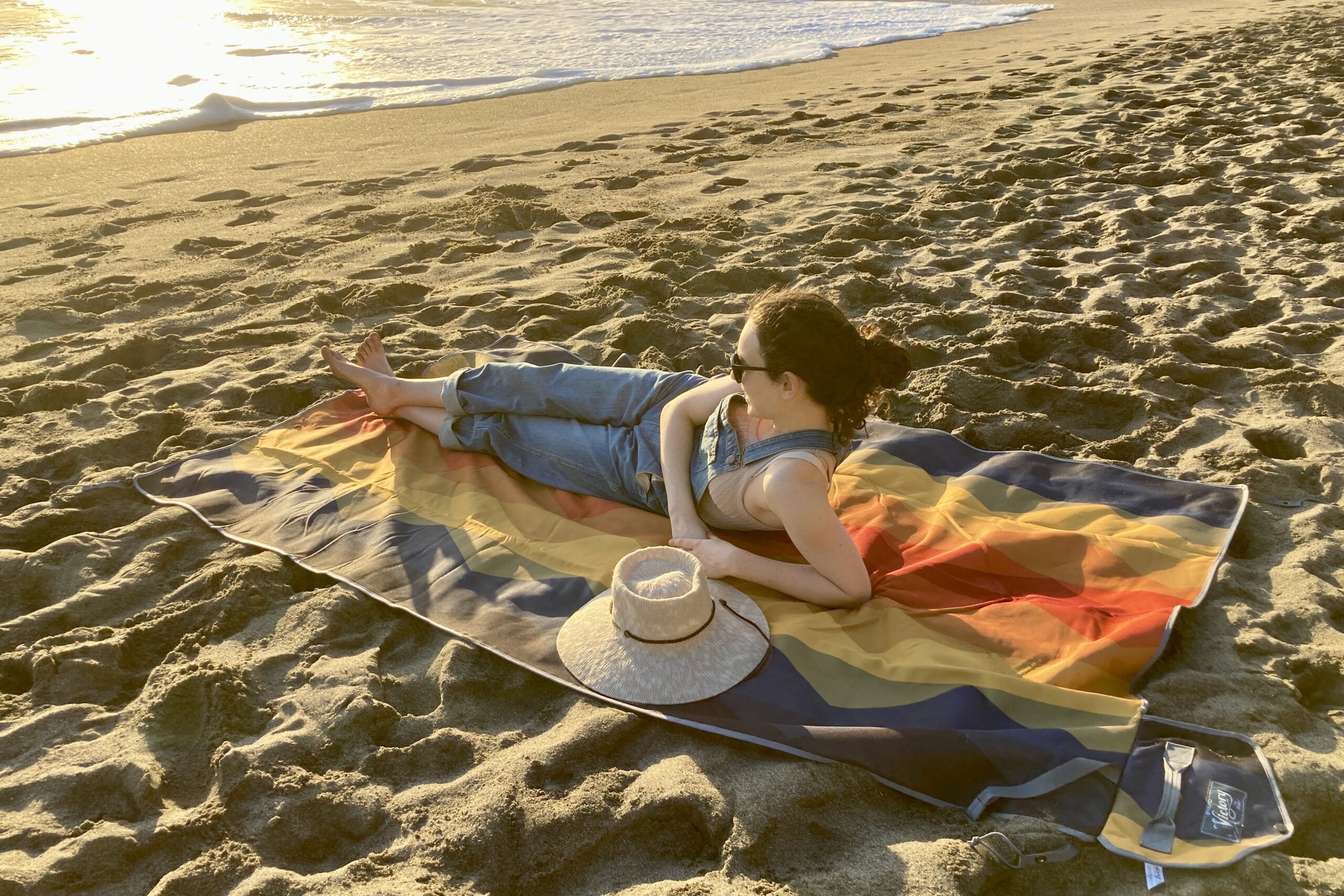 Woman laying out on the Nemo Victory Patio Blanket on the beach, gazing out at the ocean waves.