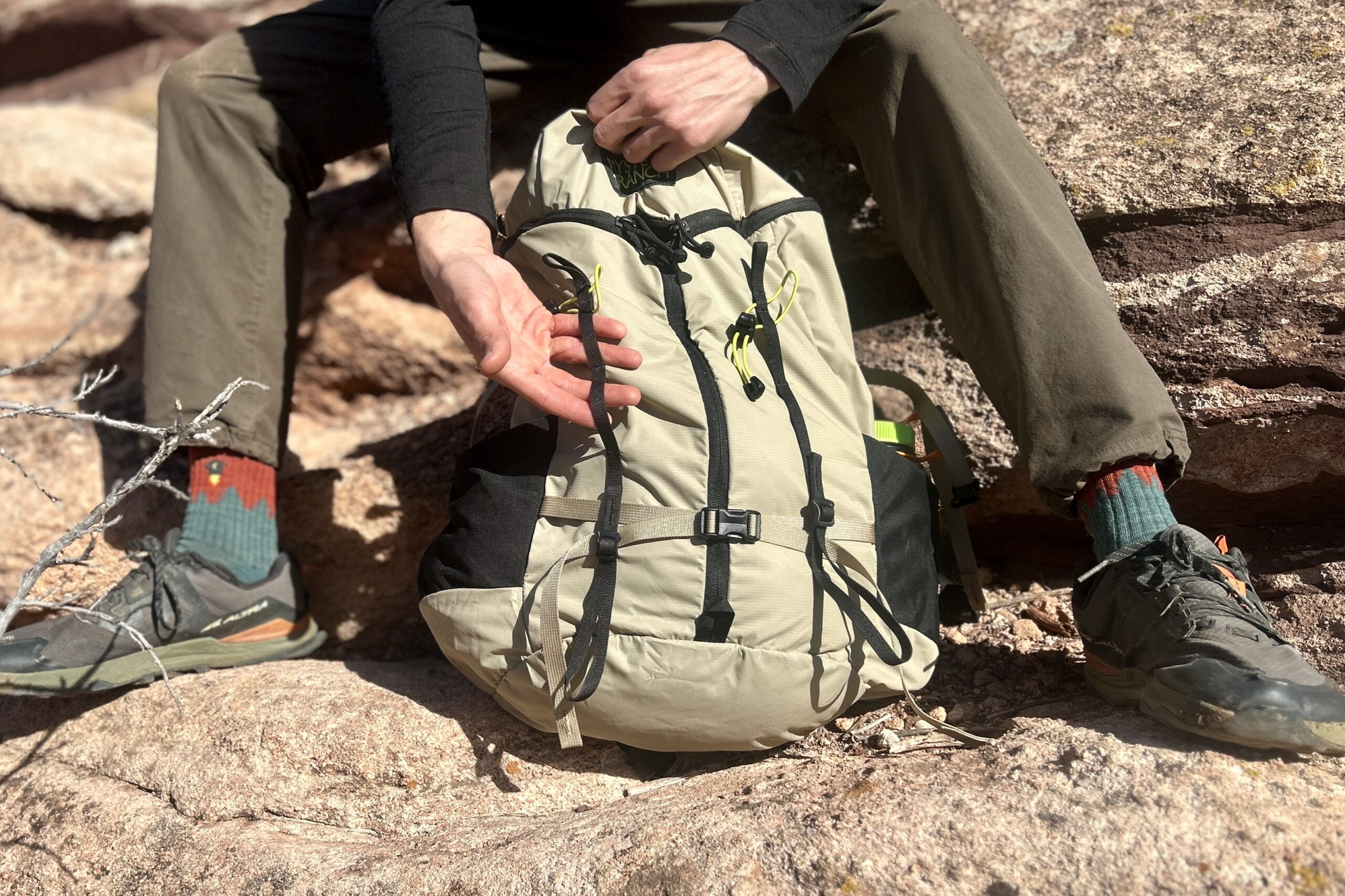 Close up of a man showing off the daisy chain on his daypack in a desert setting.