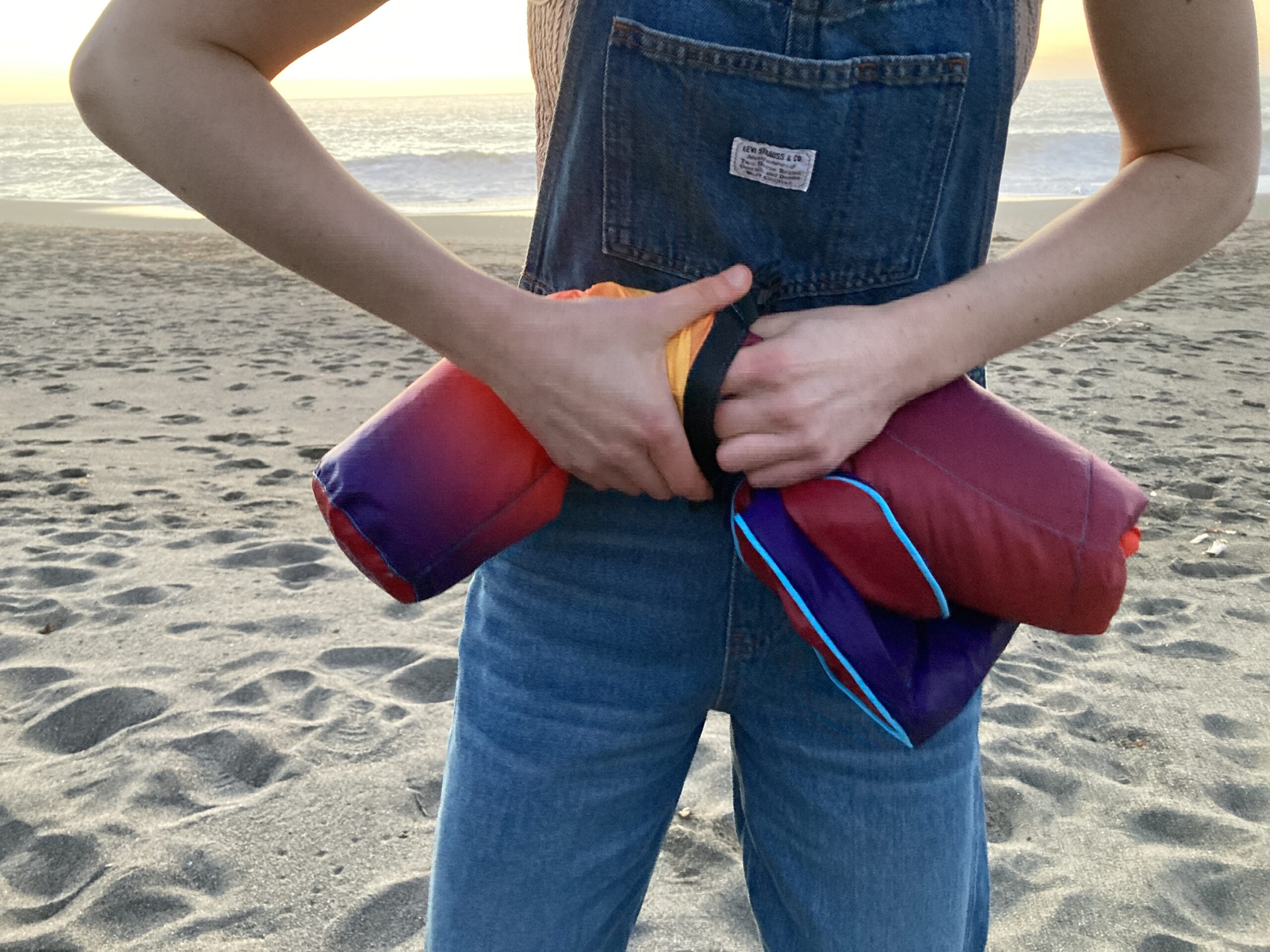 Close-up of the Rumpl NanoLoft Puffy Blanket being stuffed back into its carry case, with the ocean as a backdrop on the beach.