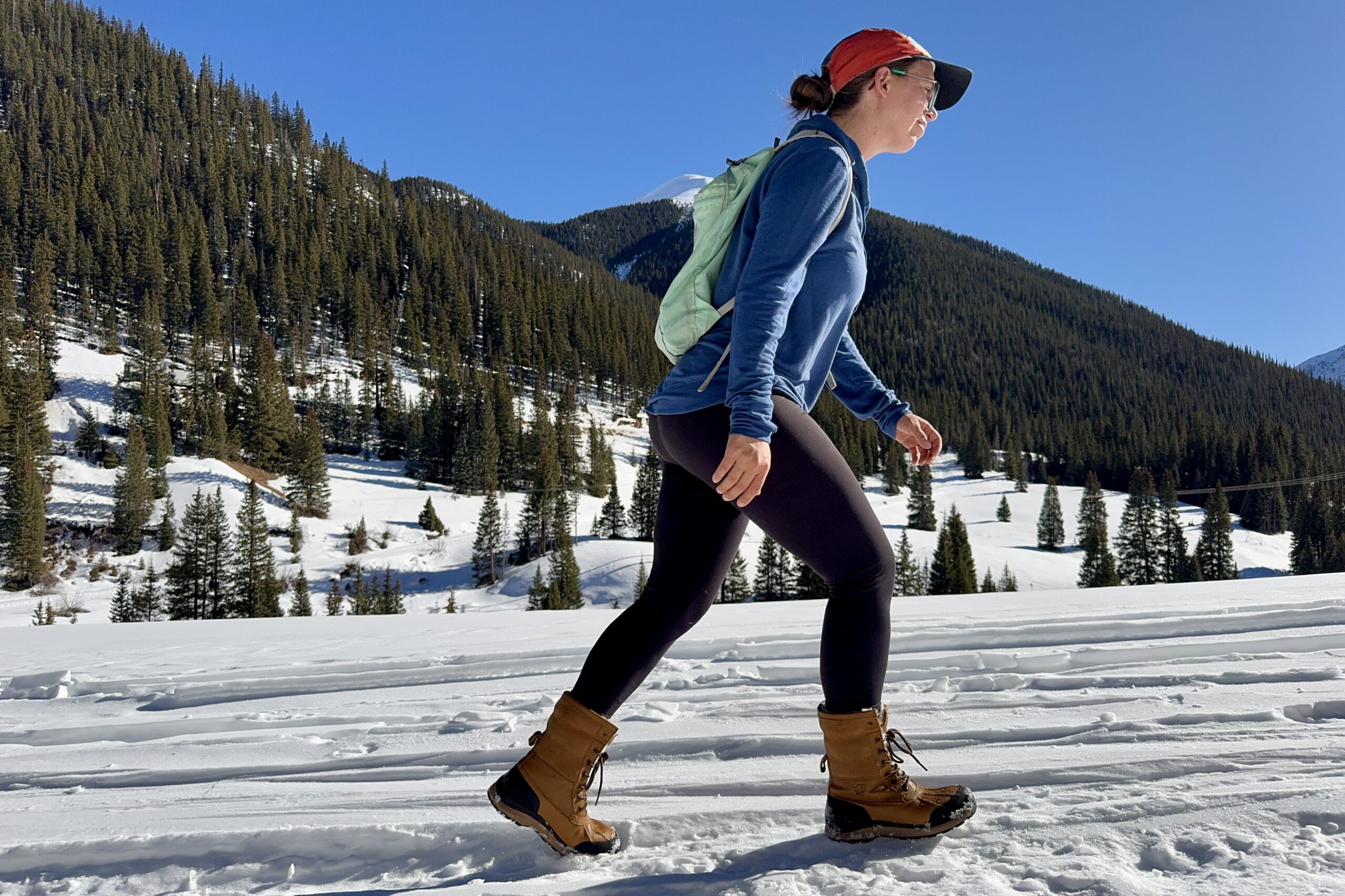 A person wearing the UGG boots is hiking in the snow in the mountains.