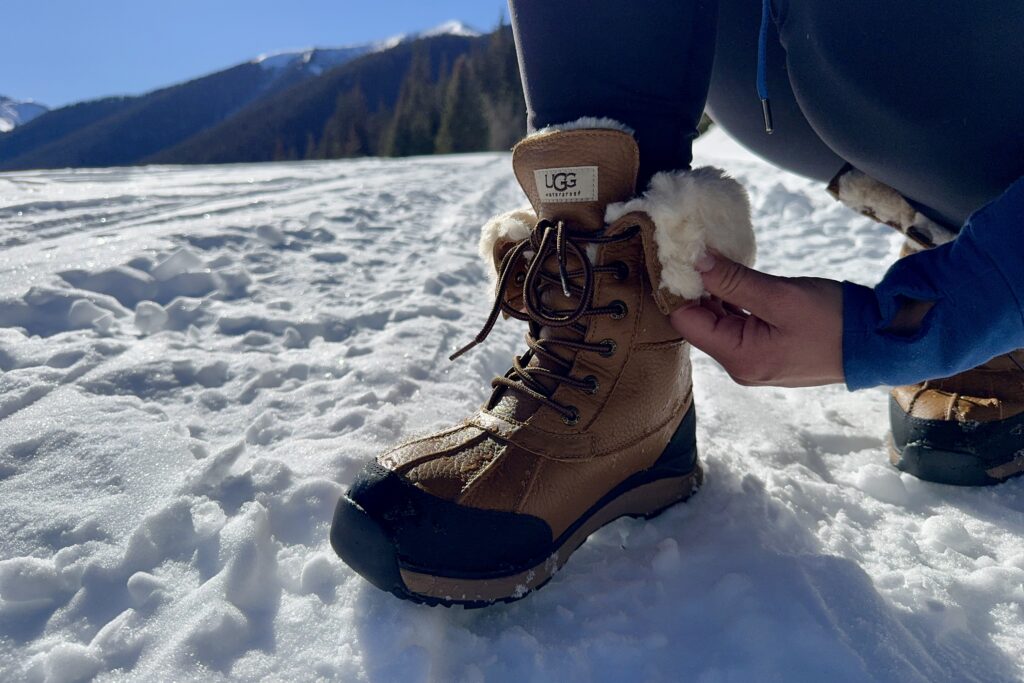 A close up of a person rolling down the top of the UGG boots in the snow.