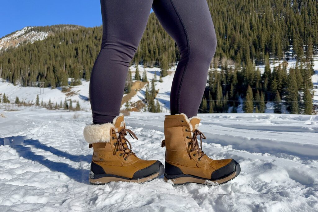 A close up of a person wearing the UGG boots in the snow. One boot is rolled up and the other is rolled down.