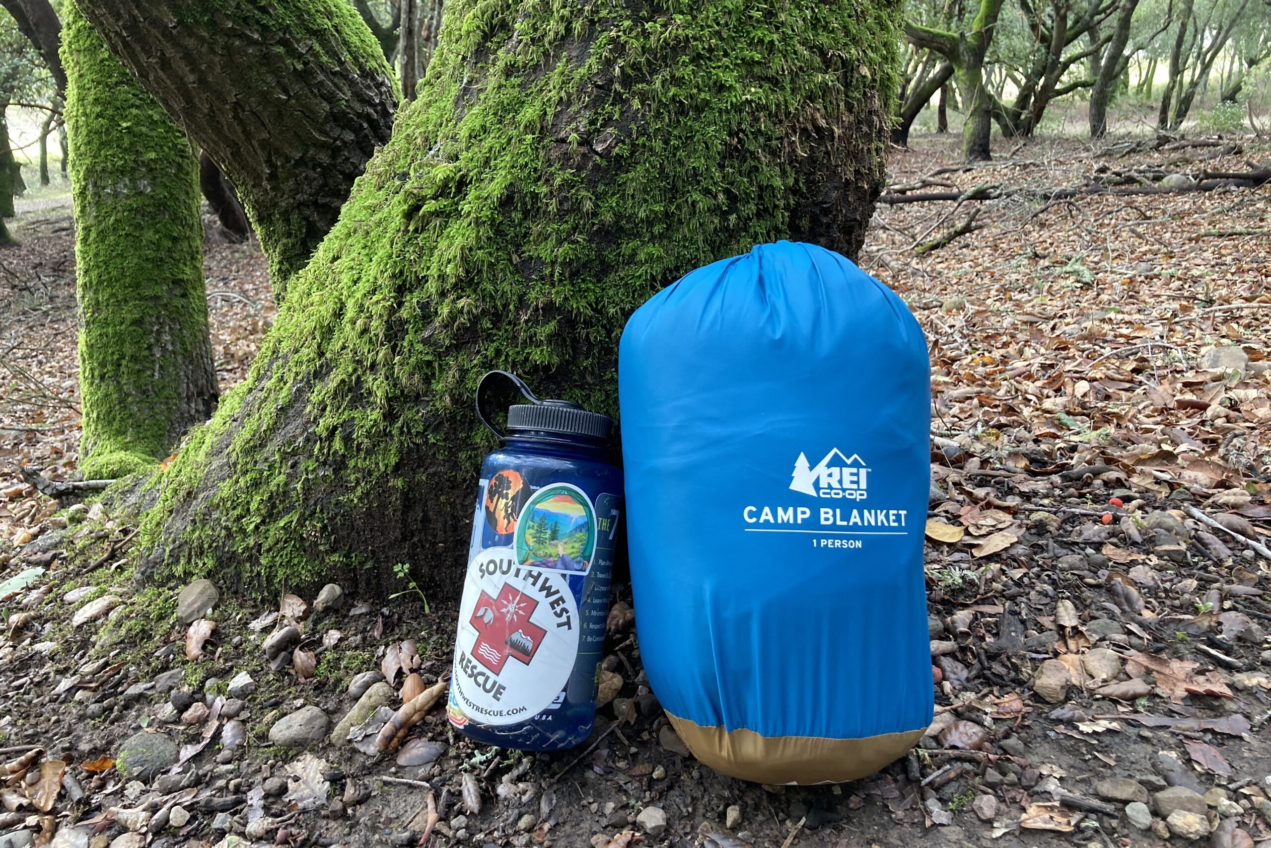 The REI Camp Blanket packed in its stuff sack next to a Nalgene.