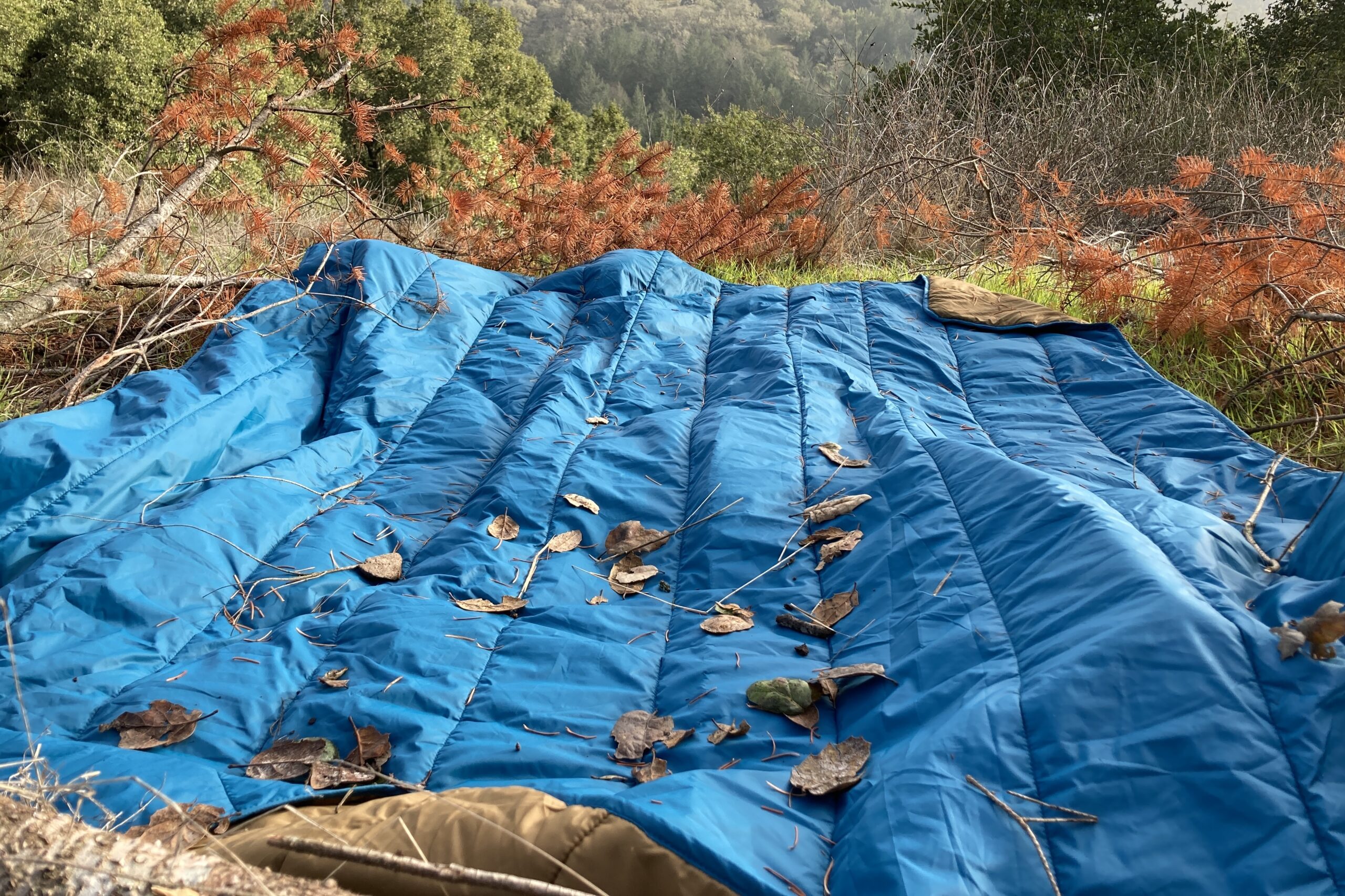 The REI camp blanket laid out on the ground covered in debris.