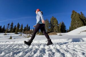 A person walking in the snow while wearing the Minx Shorty boots in the woods.