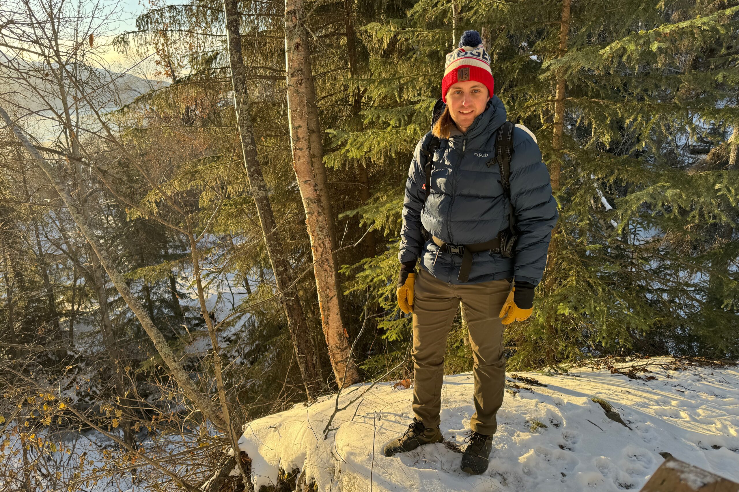 A man stands on a snowy trail at sunset.