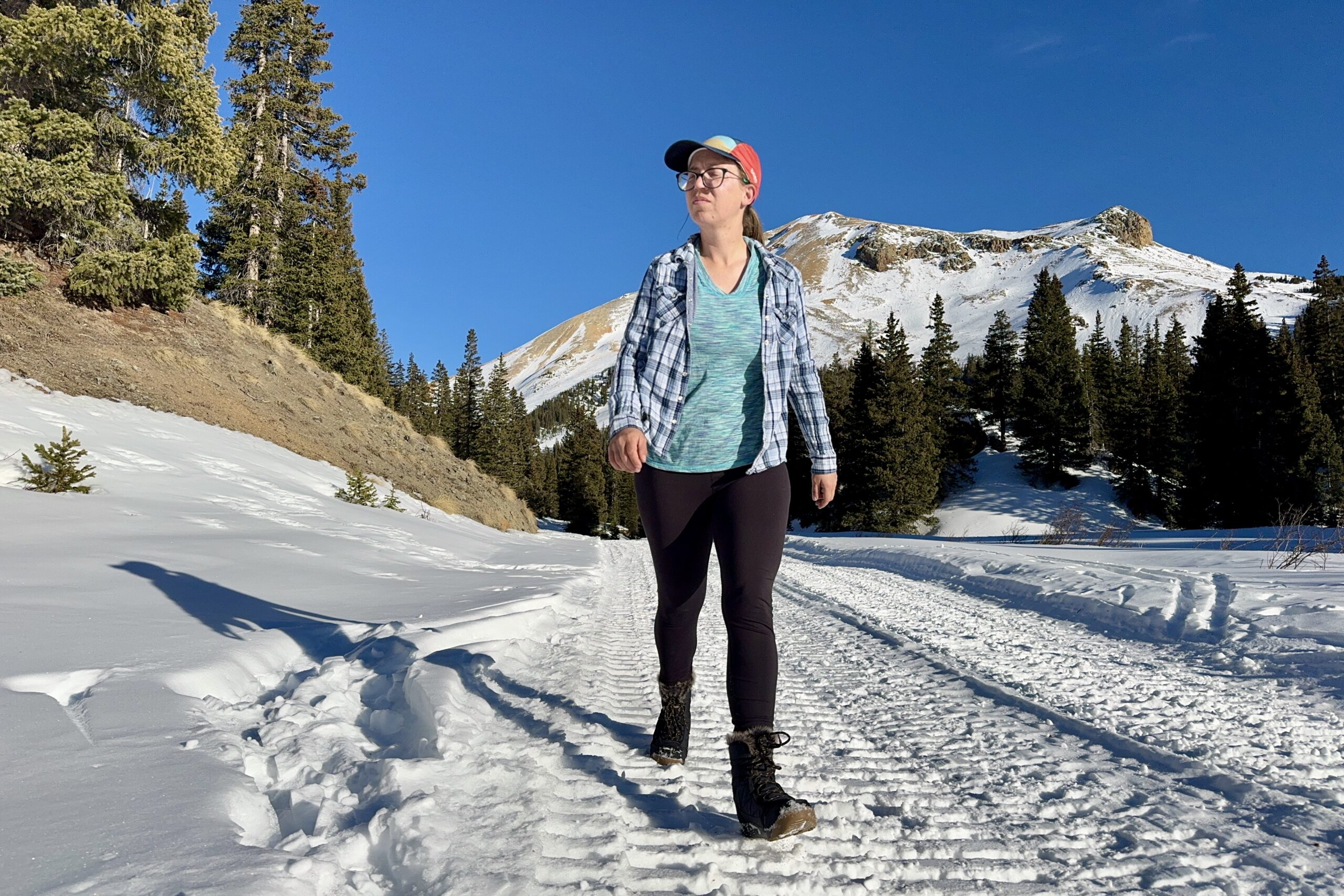 A person walking in the snow while wearing the Minx Shorty boots in the mountains.