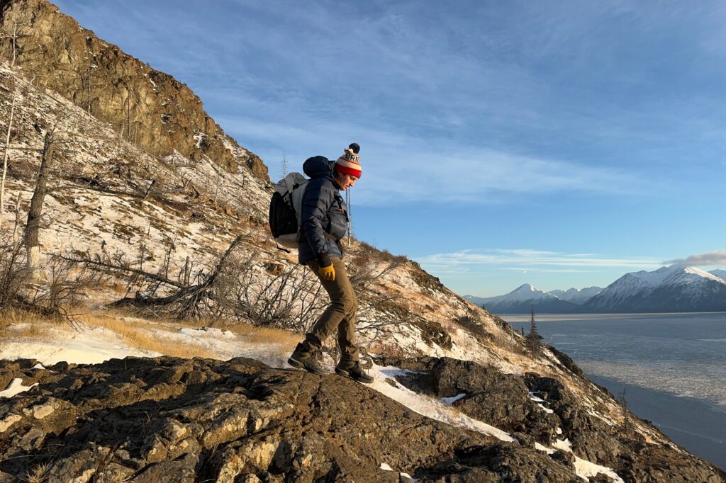 A man walks down a rocky slope above an ocean view