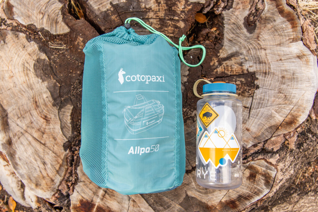 The Cotopaxi Allpa 50 Duffel packed into it's storage sack and placed next to a Nalgene for size reference.