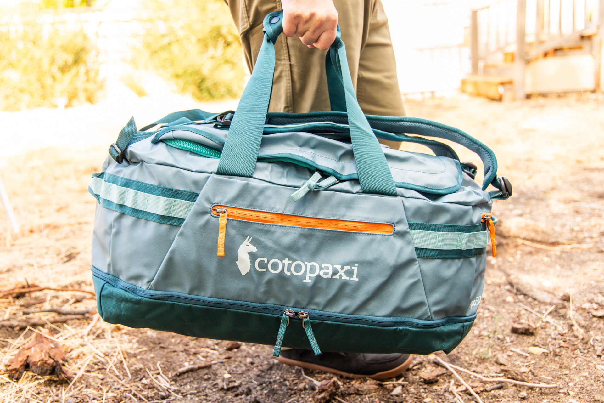 A man carries the Cotopaxi Allpa 50 duffel using the top duffel handles.