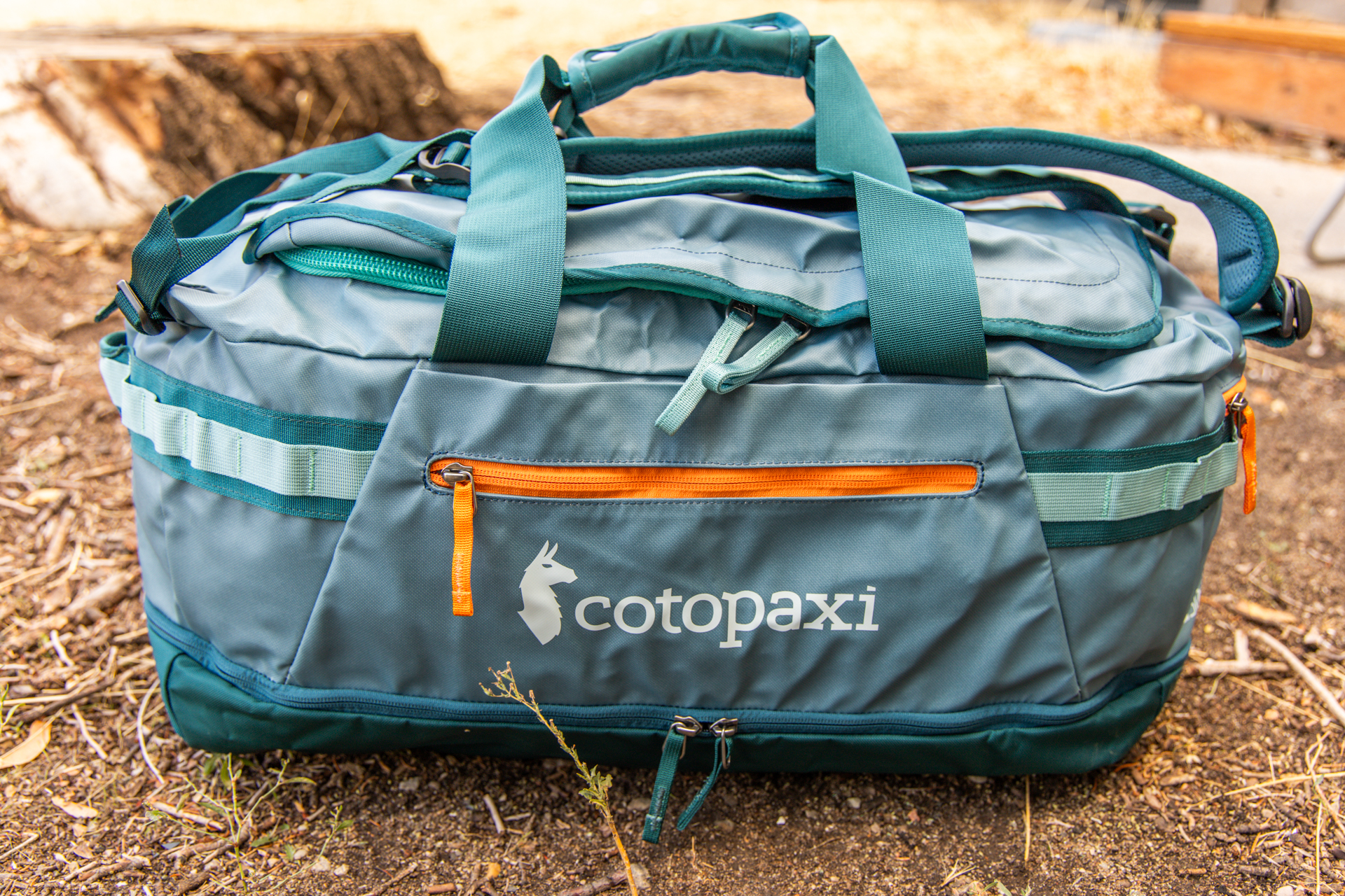 A side views of the Cotopaxi Allpa 50L duffel and its bottom zipper compartment, side and end zipper pockets, handle stash pocket, and grab handles and pack straps deployed.