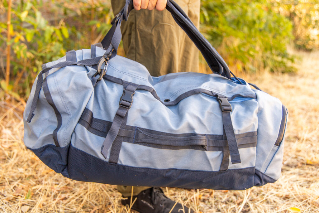 A man carries the Eagle Creek Cargo Hauler 60L duffel by its combination backpack straps and grab handles.