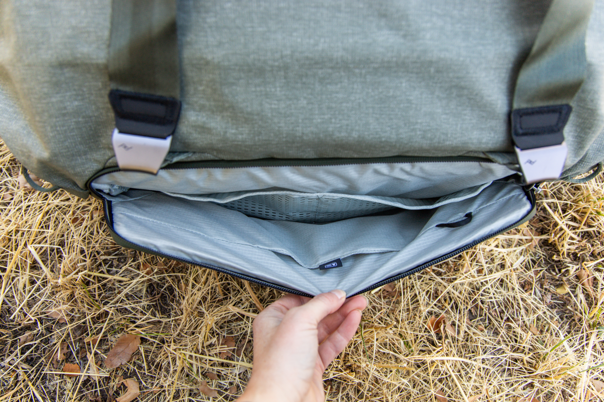 A hand opens the larger external pocket to reveal several more drop pockets within.