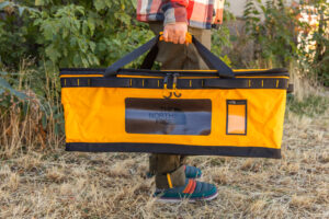 A man carries the Gear Box using the duffel handles on top of the bag.