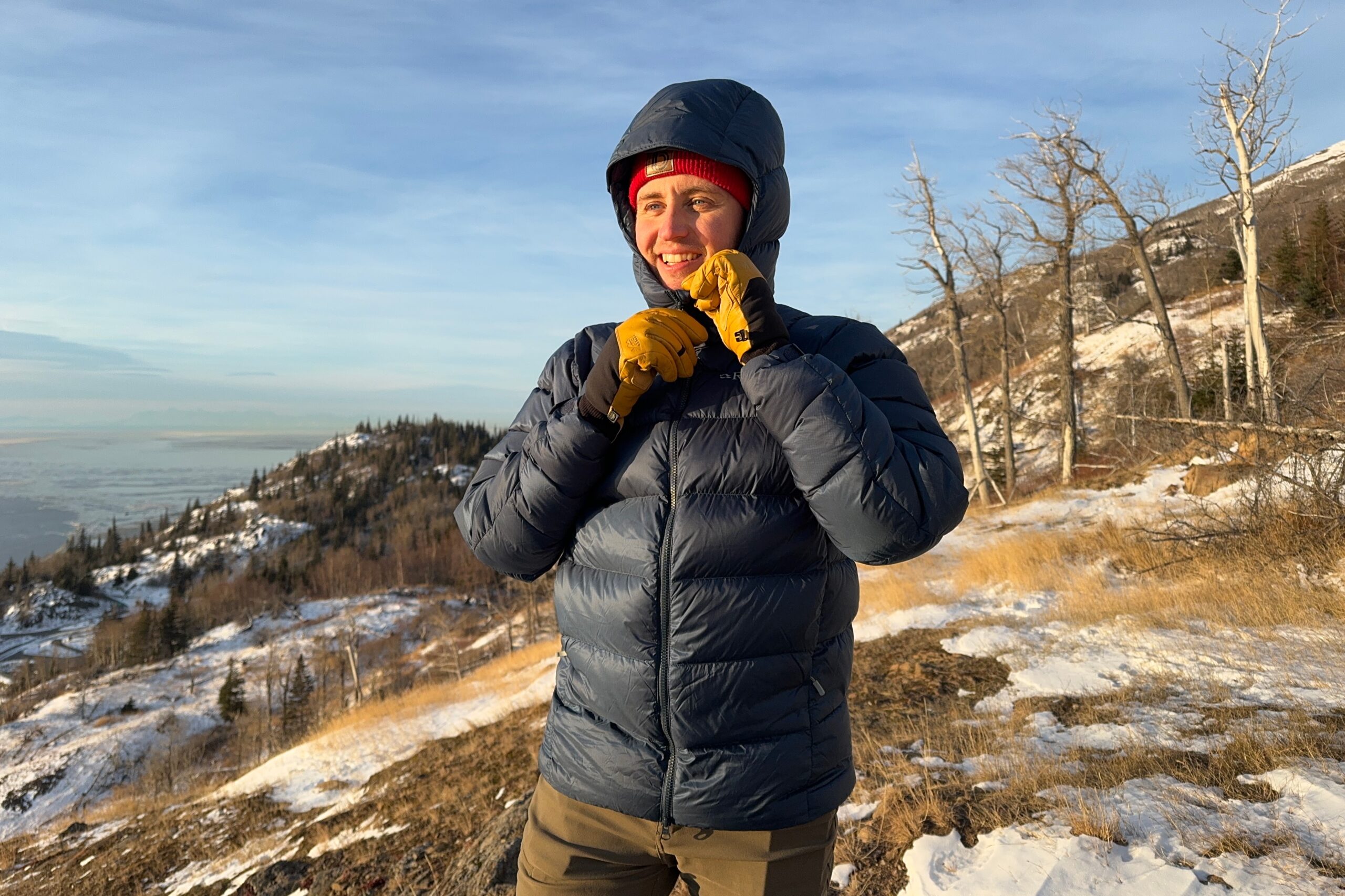 A man zips up his down jacket at sunset