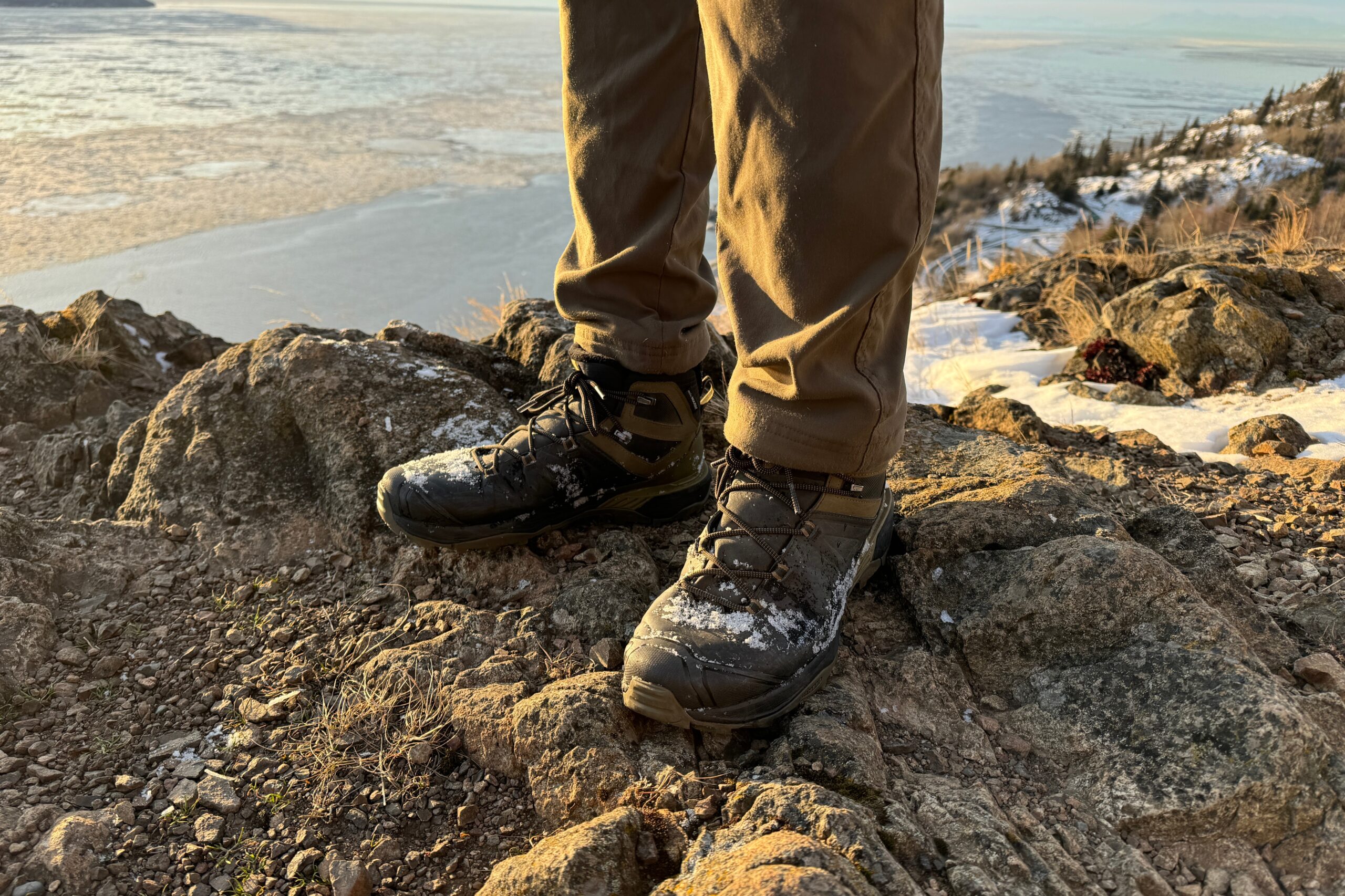 A closeup of snow covered boots standing on a rocky outcrop.