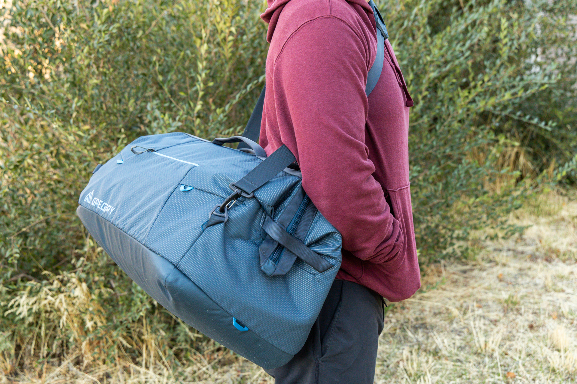 A man hand-holds the Gregory Alpaca Wide Mouth 50 duffel using the removable over-the-shoulder strap.