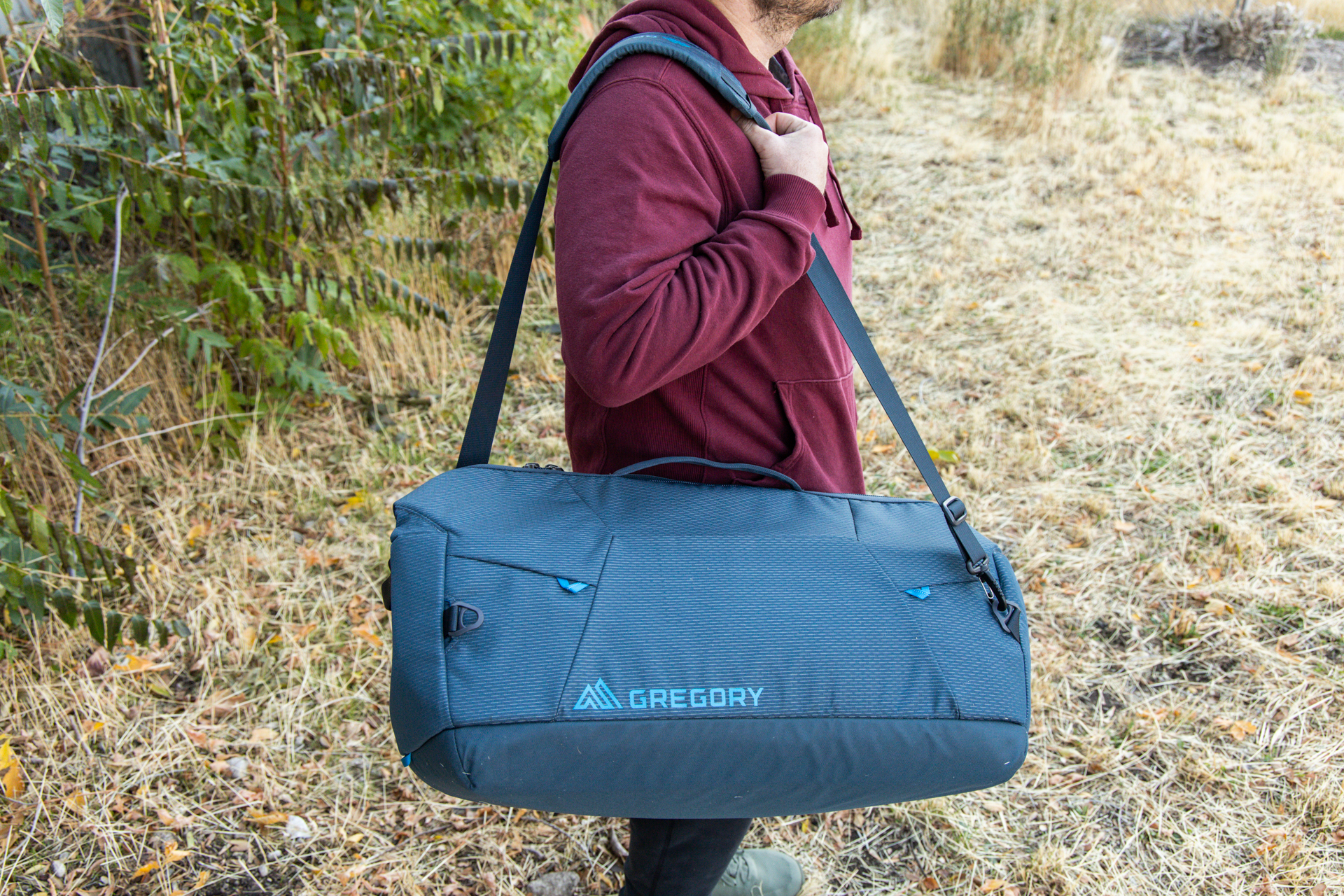 A man hand-holds the Gregory Alpaca Wide Mouth 50 duffel using the removable over-the-shoulder strap.