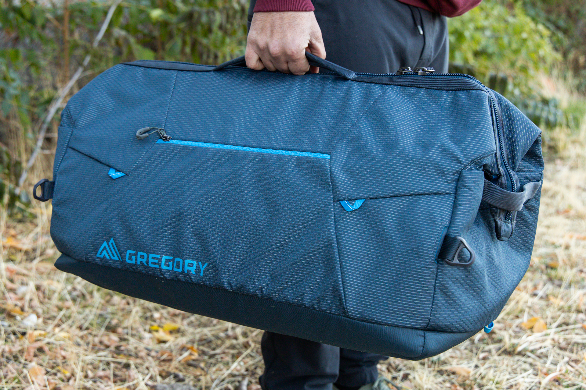 A man hand-holds the Gregory Alpaca Wide Mouth 50 duffel using the low-profile top grab handles.